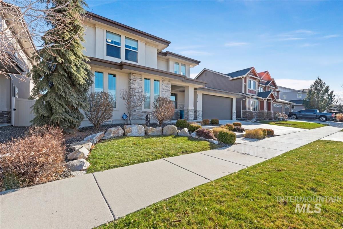 Prairie-style home with stucco siding, a garage, stone siding, a front lawn, and a residential view