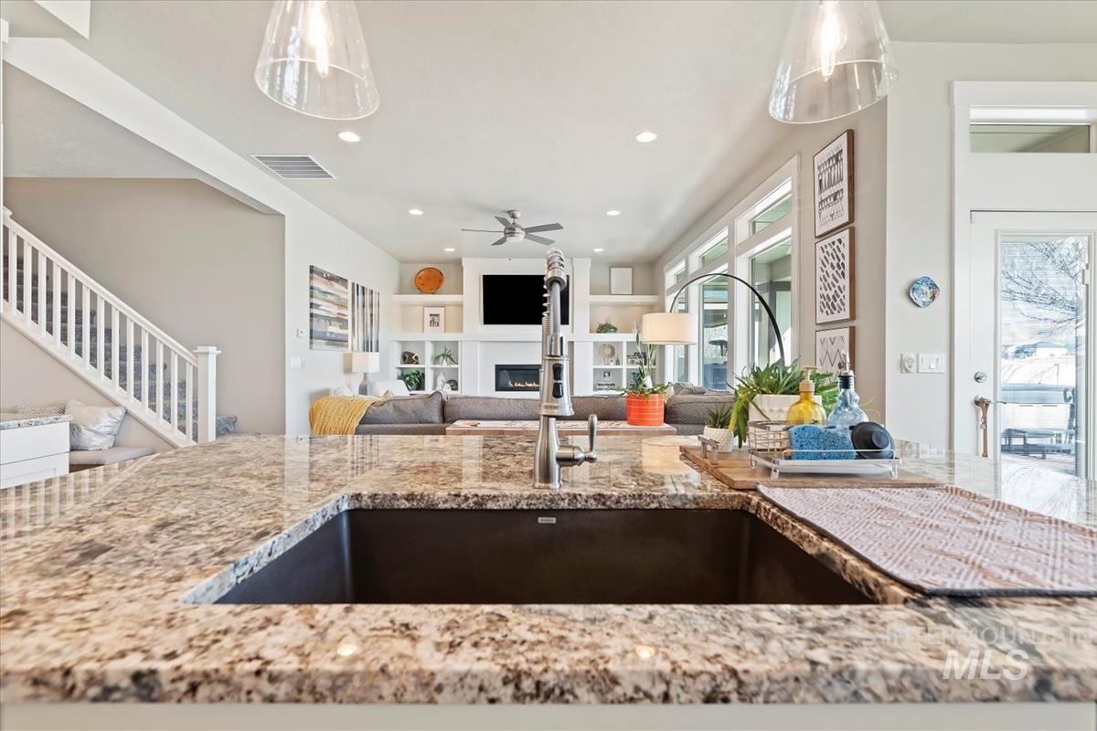 Kitchen featuring a glass covered fireplace, light stone counters, open floor plan, pendant lighting, and recessed lighting