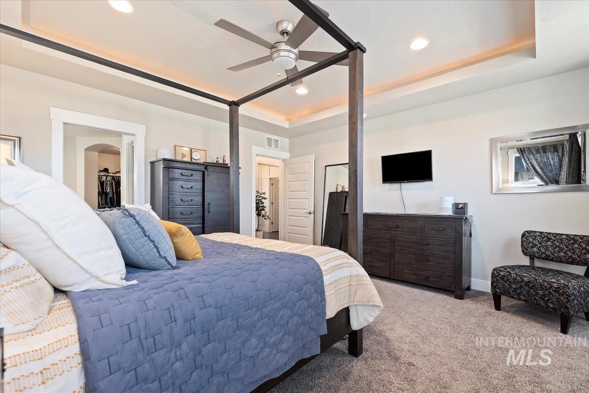 Carpeted bedroom featuring a tray ceiling, ceiling fan, a walk in closet, and recessed lighting