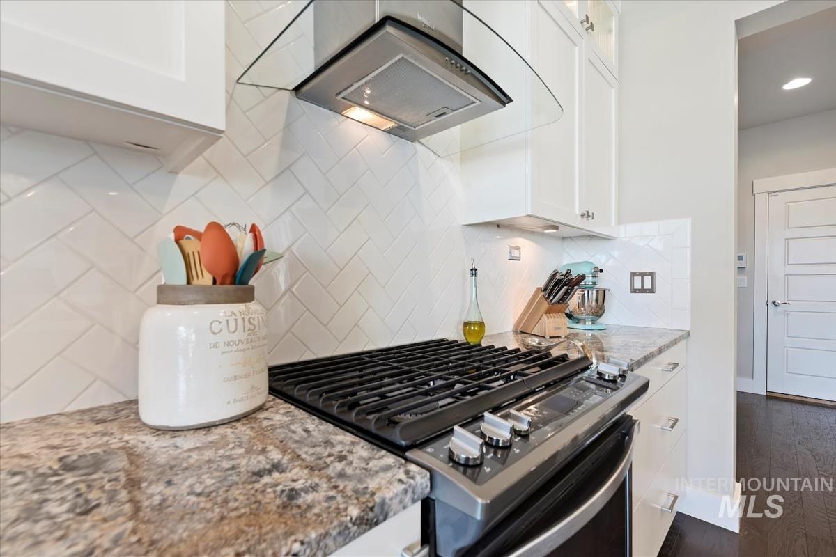 Kitchen with light stone counters, stainless steel gas stove, and white cabinets