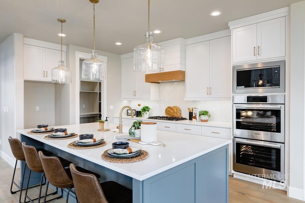 Kitchen with decorative backsplash, white cabinetry, appliances with stainless steel finishes, pendant lighting, and a kitchen island with sink