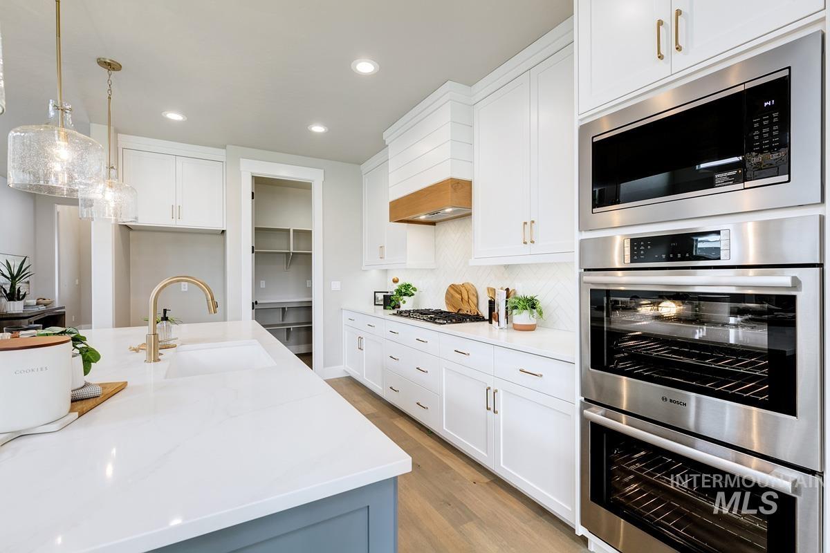 Kitchen featuring stainless steel appliances, light stone counters, decorative light fixtures, white cabinetry, and recessed lighting