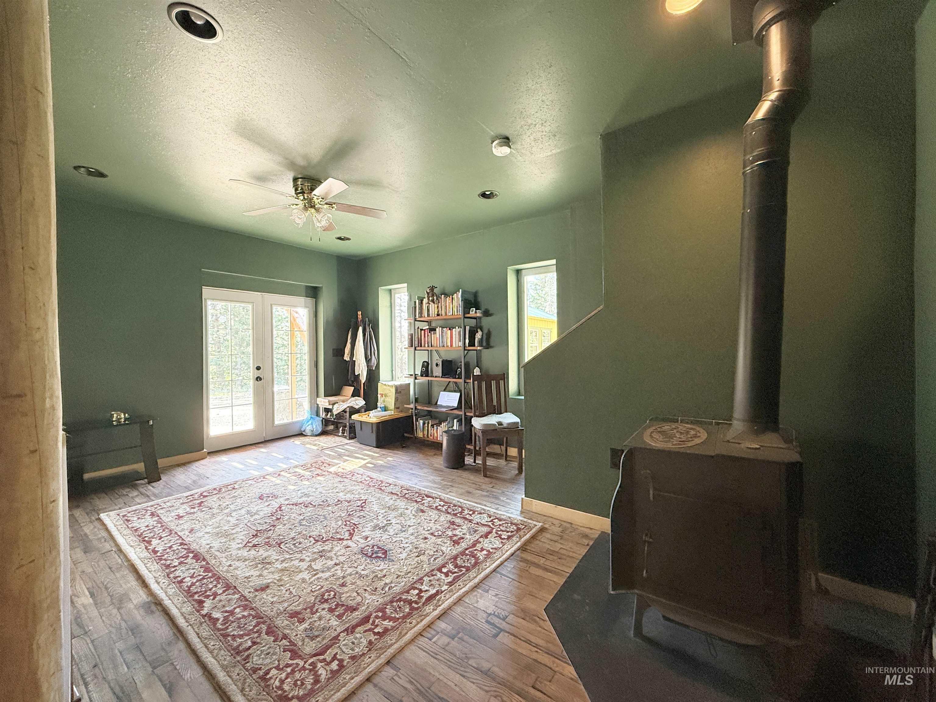 Office with a wood stove, a ceiling fan, a textured ceiling, hardwood / wood-style floors, and french doors