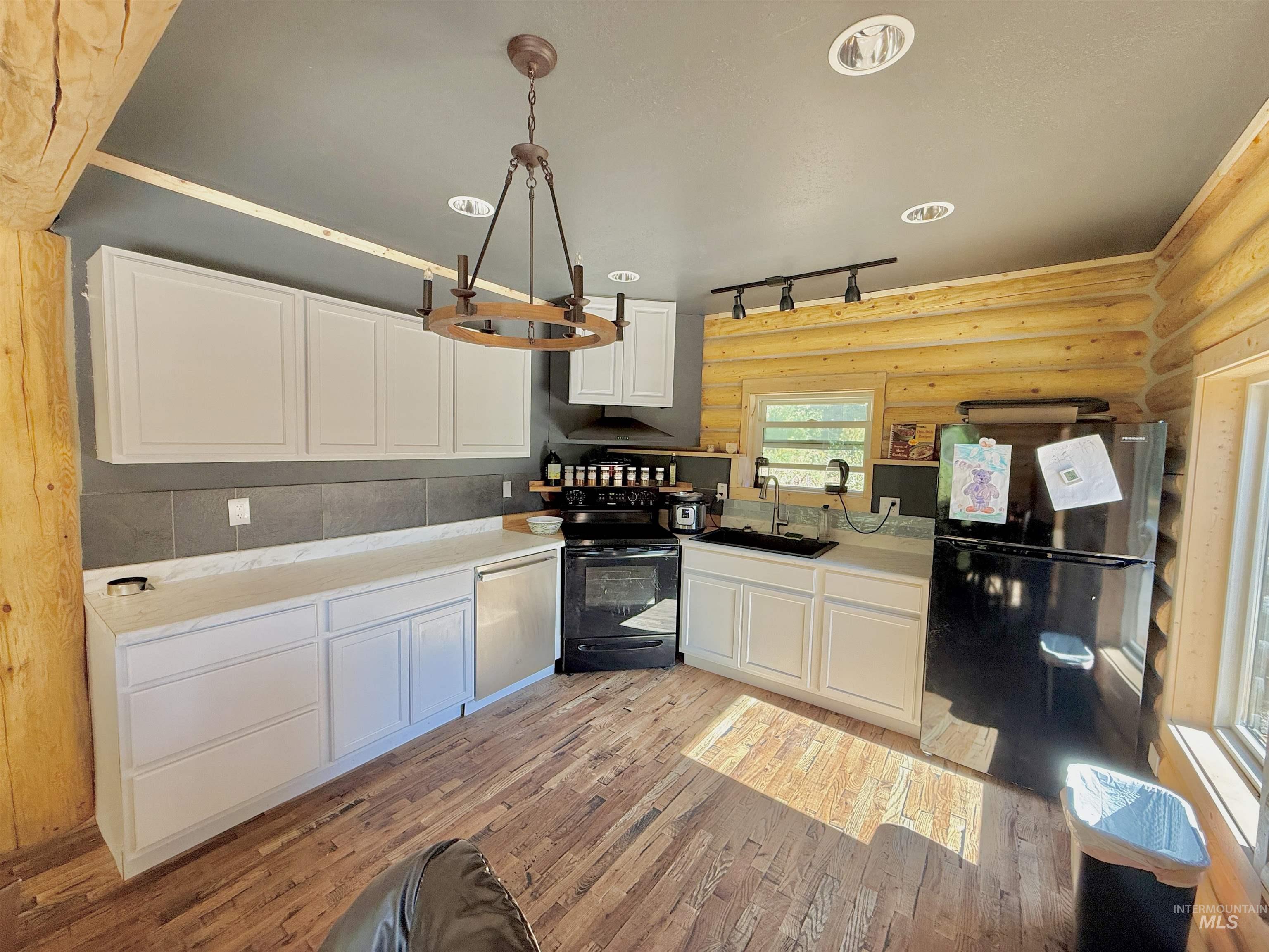 Kitchen featuring freestanding refrigerator, white cabinets, black electric range, light wood finished floors, and track lighting