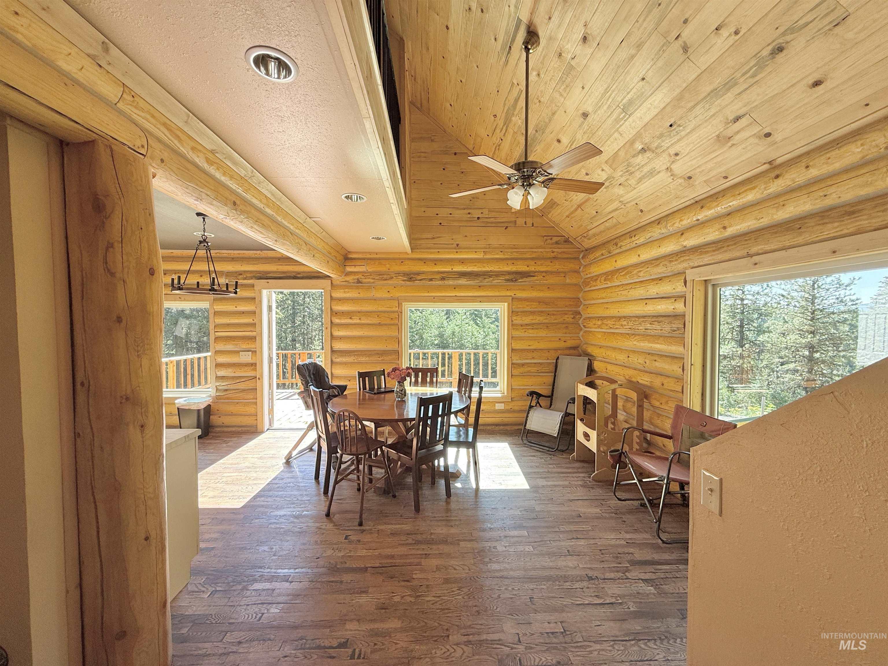 Dining area with lofted ceiling, ceiling fan, dark wood-style flooring, wood ceiling, and log walls