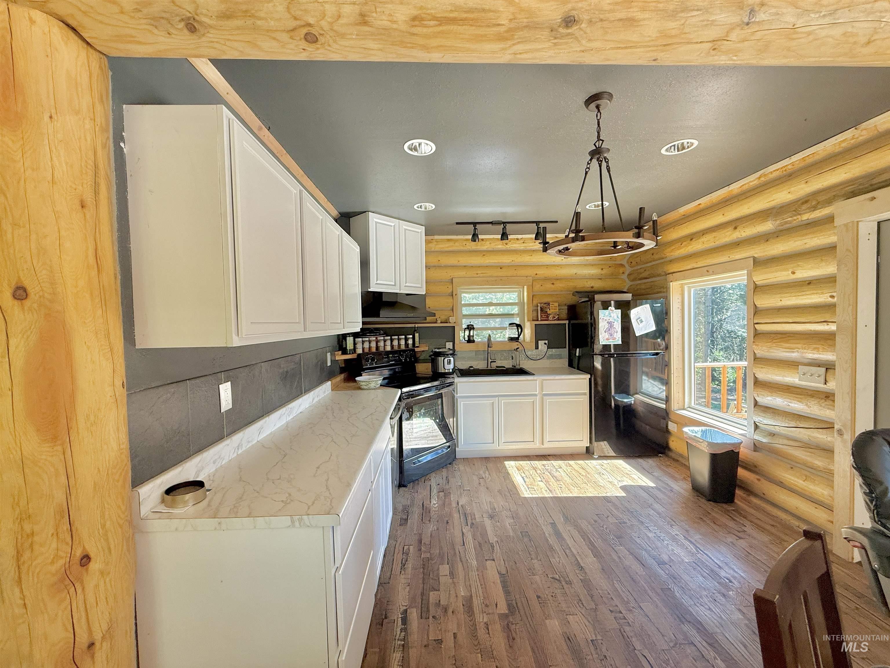 Kitchen with white cabinetry, wood finished floors, black appliances, light countertops, and log walls