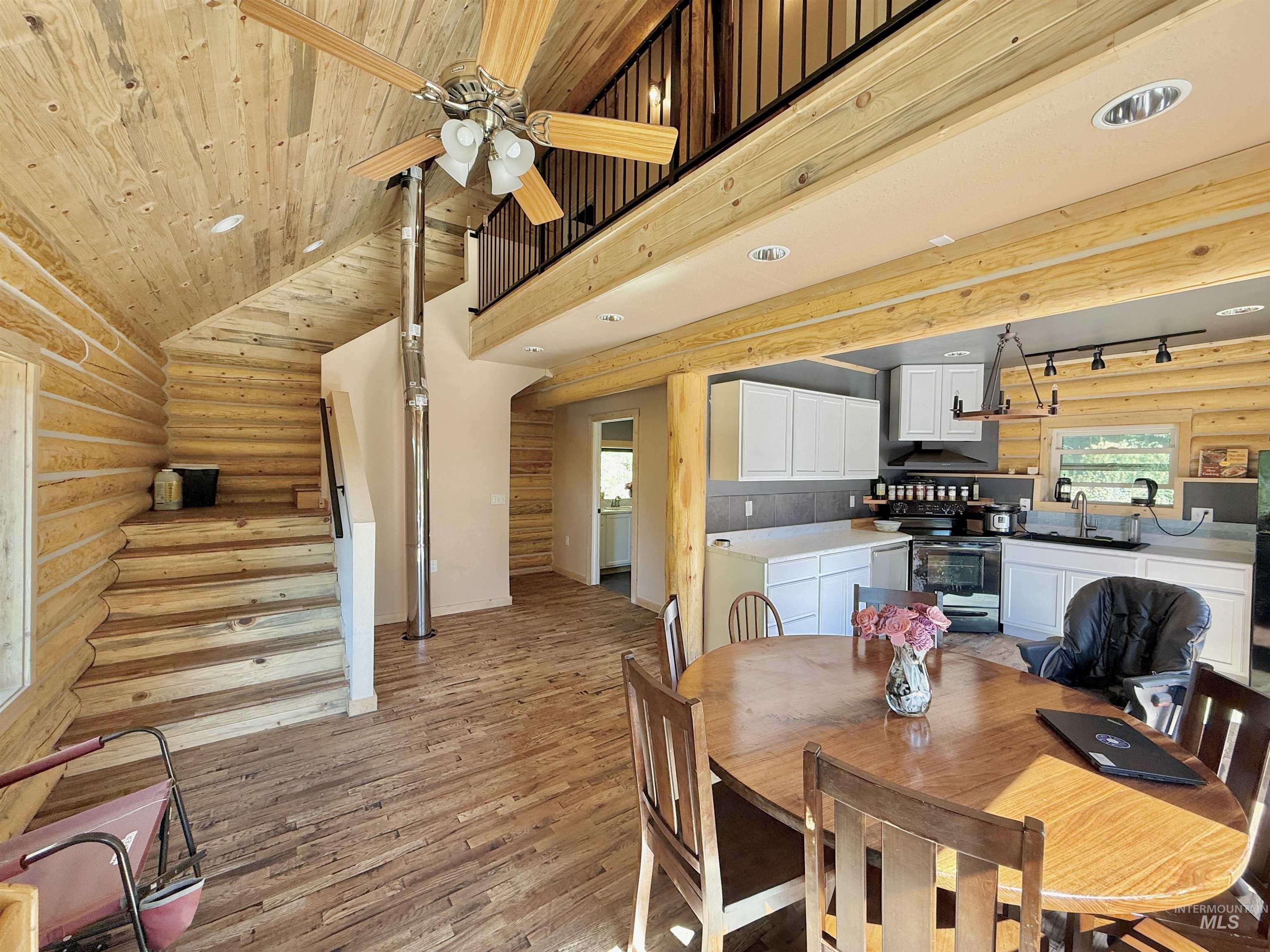 Dining space featuring rustic walls, light wood-style floors, stairway, ceiling fan, and wooden ceiling