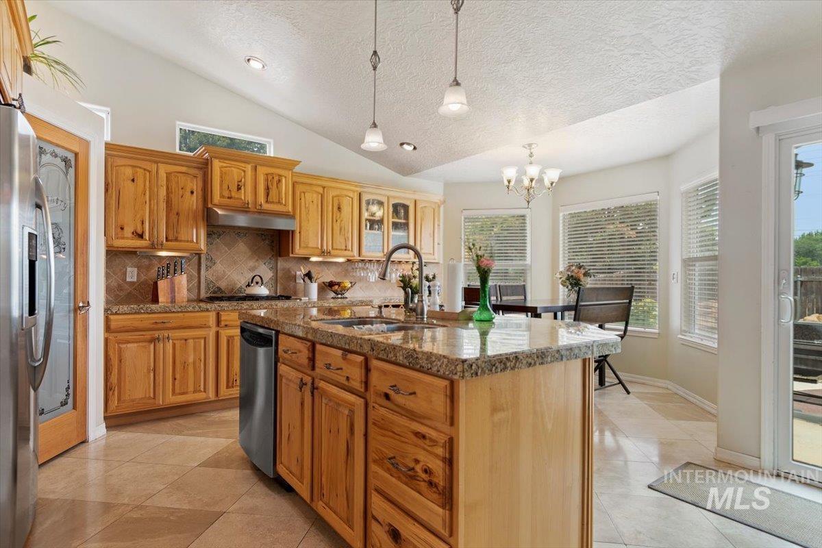 Kitchen with light tile patterned floors, glass fronted cabinets, a center island with sink, and stainless steel appliances