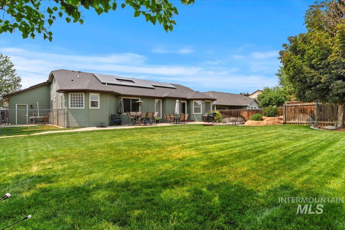 Back of house featuring roof mounted solar panels, a fenced backyard, a patio area, and roof with shingles