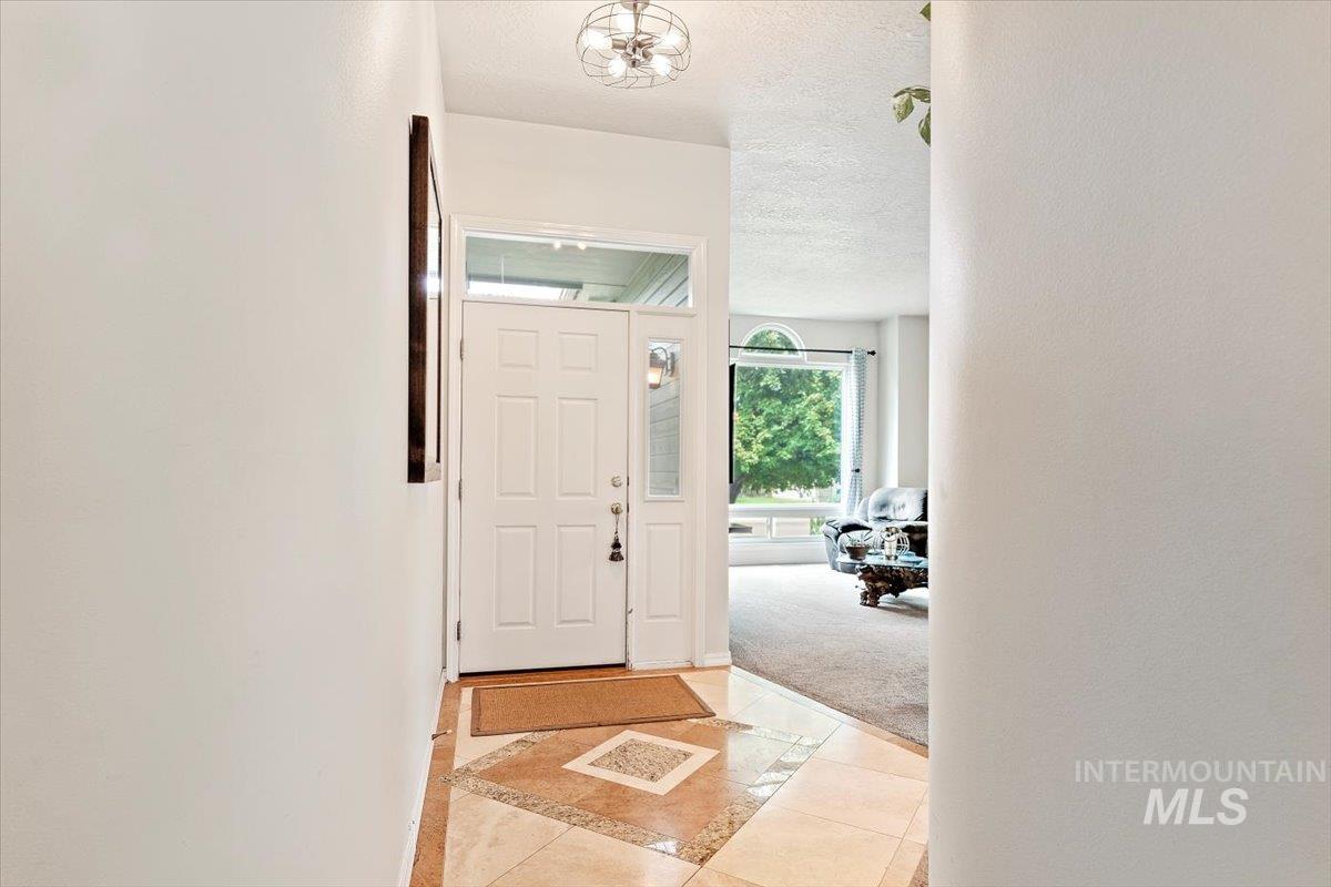 Foyer featuring inlaid floor details, light tile patterned flooring, a textured ceiling, and light colored carpet