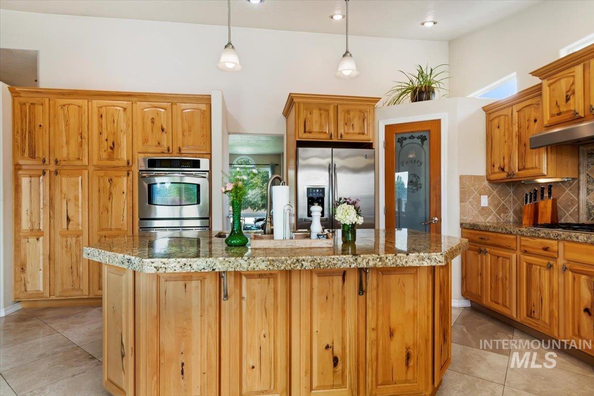 Kitchen with stainless steel appliances, an island with sink, backsplash, hanging light fixtures, and light tile patterned flooring