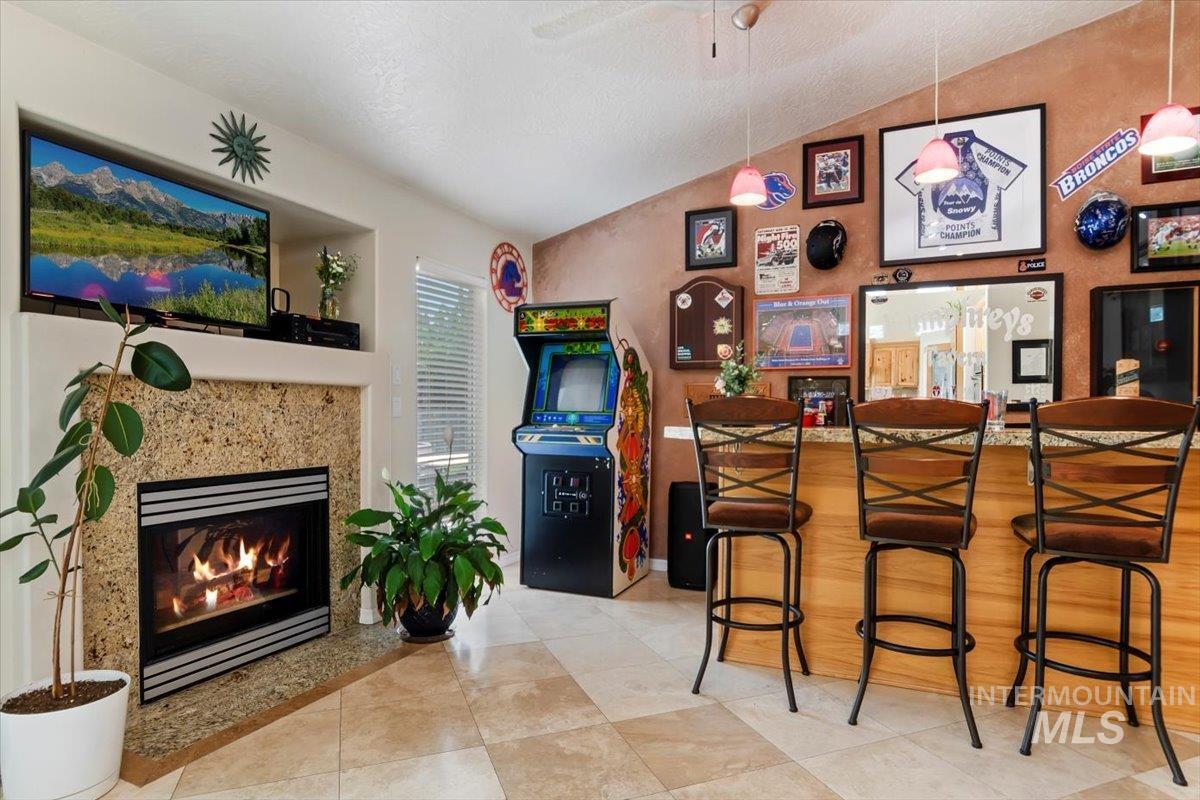 Bar area with vaulted ceiling, a fireplace, ceiling fan, and light tile patterned floors