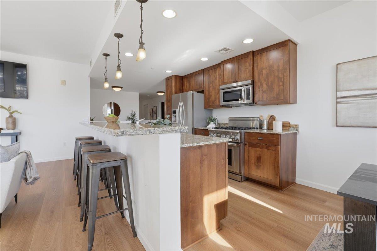 Kitchen with light stone counters, light wood-style floors, stainless steel appliances, and a breakfast bar area