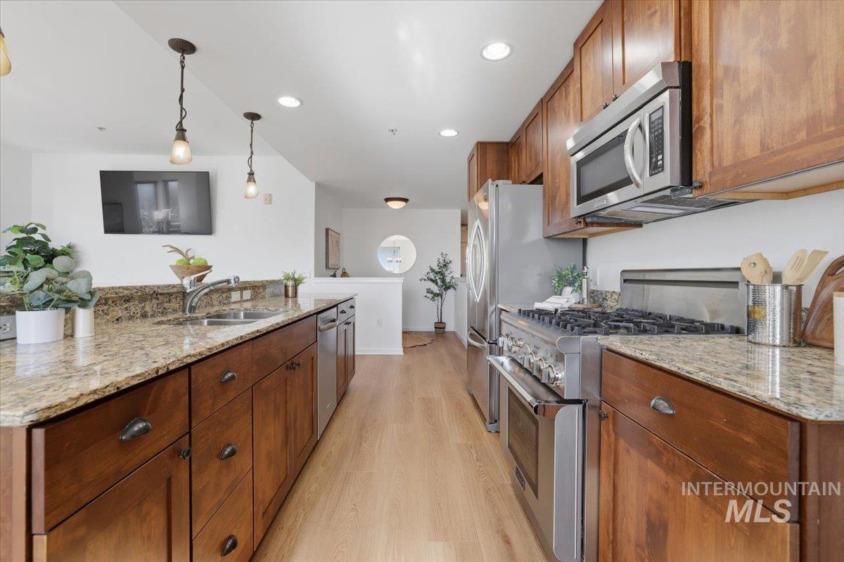 Kitchen featuring light stone counters, stainless steel appliances, light wood-style flooring, and wood finish cabinets