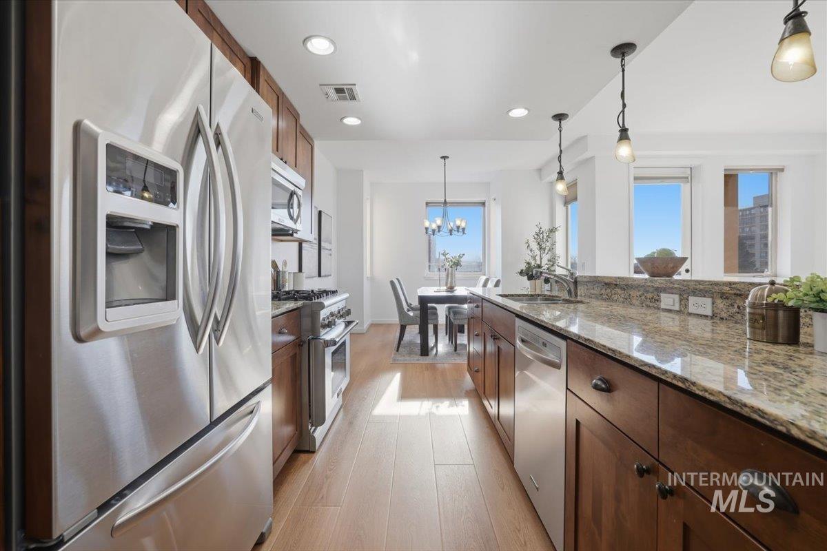 Kitchen featuring stainless steel appliances, light stone countertops, light wood-type flooring, and wood finish cabinetry