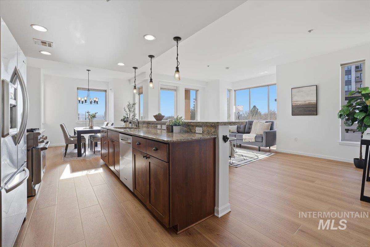 Kitchen featuring dark stone countertops, stainless steel appliances, a kitchen island with sink, light wood-type flooring, and decorative light fixtures