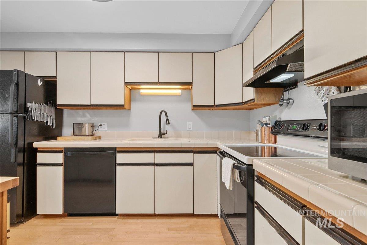 Kitchen with black appliances, light wood-type flooring, and under cabinet range hood