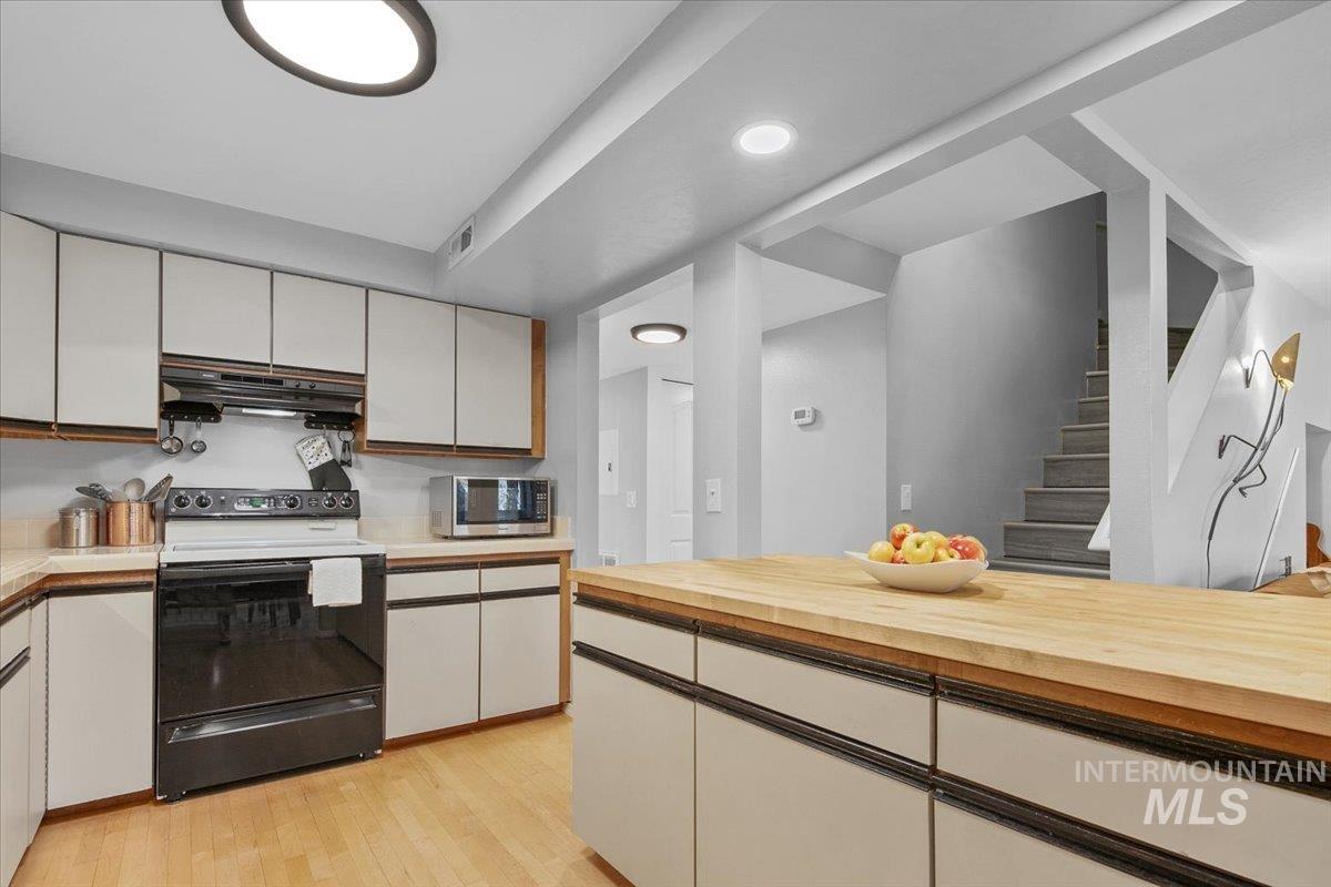 Kitchen with black range with electric cooktop, white cabinetry, light wood-style flooring, under cabinet range hood, and stainless steel microwave