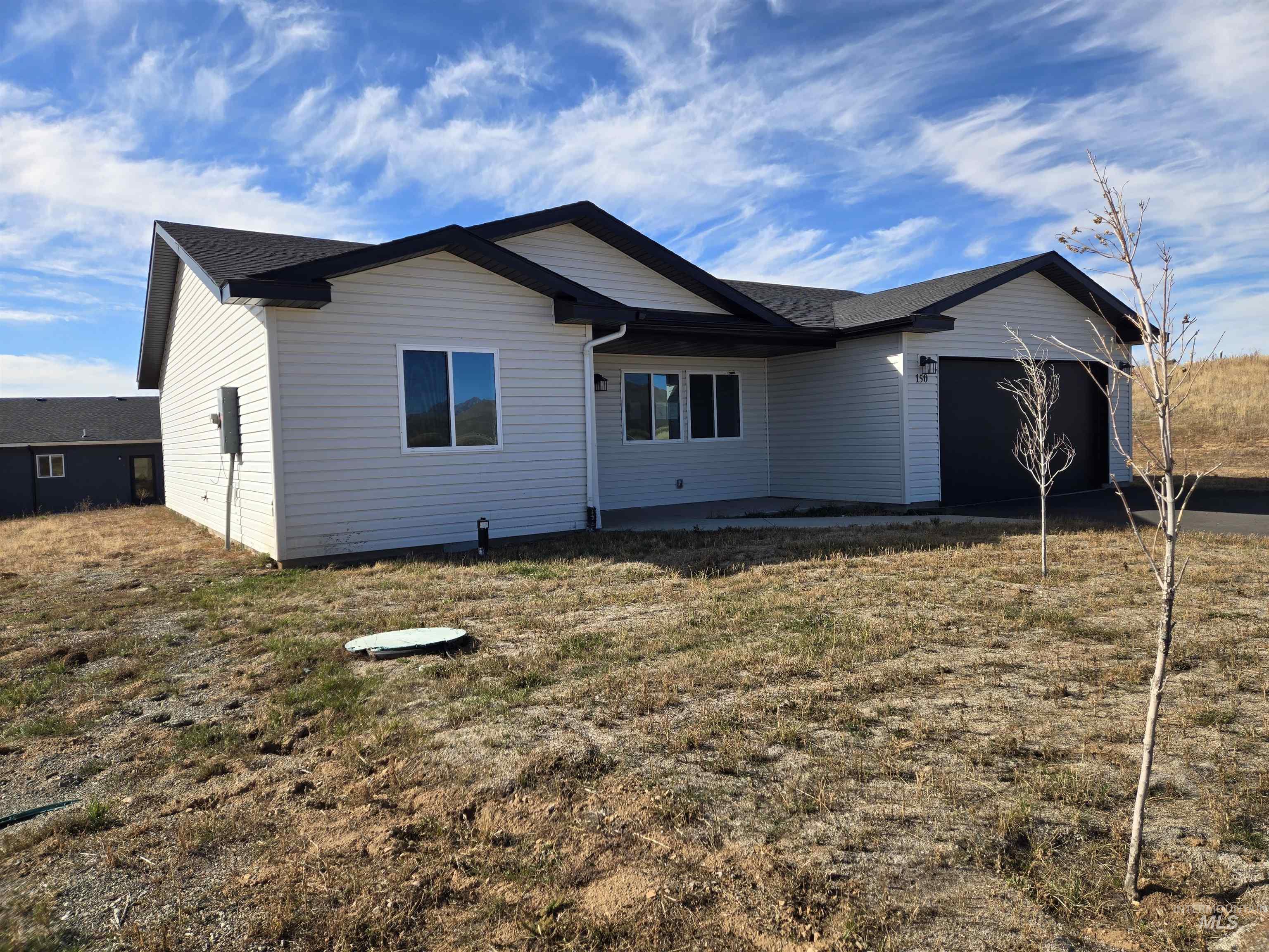 Rear view of property with an attached garage, a patio area, and a lawn