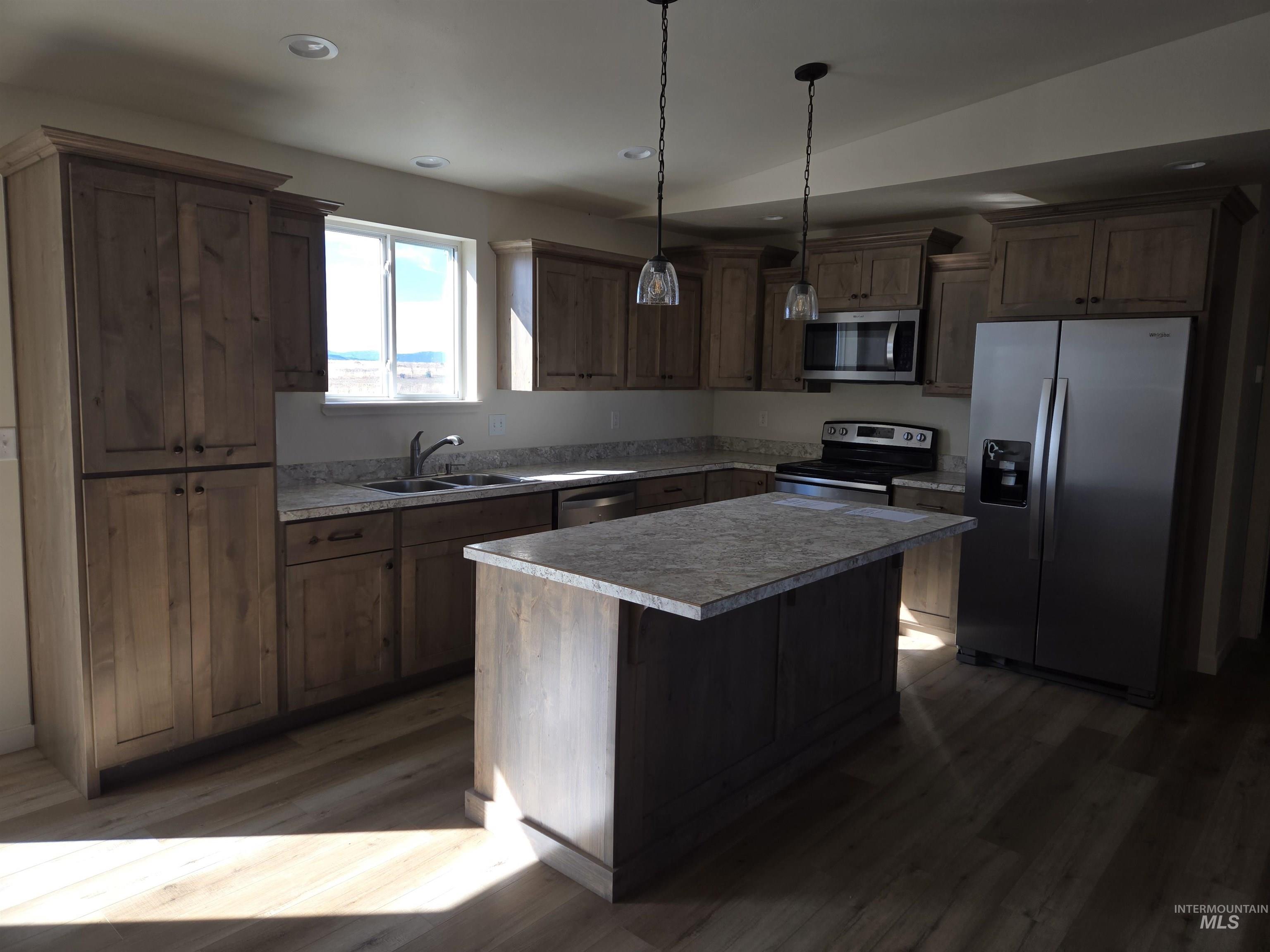 Kitchen featuring appliances with stainless steel finishes, dark wood-type flooring, hanging light fixtures, a center island, and light countertops