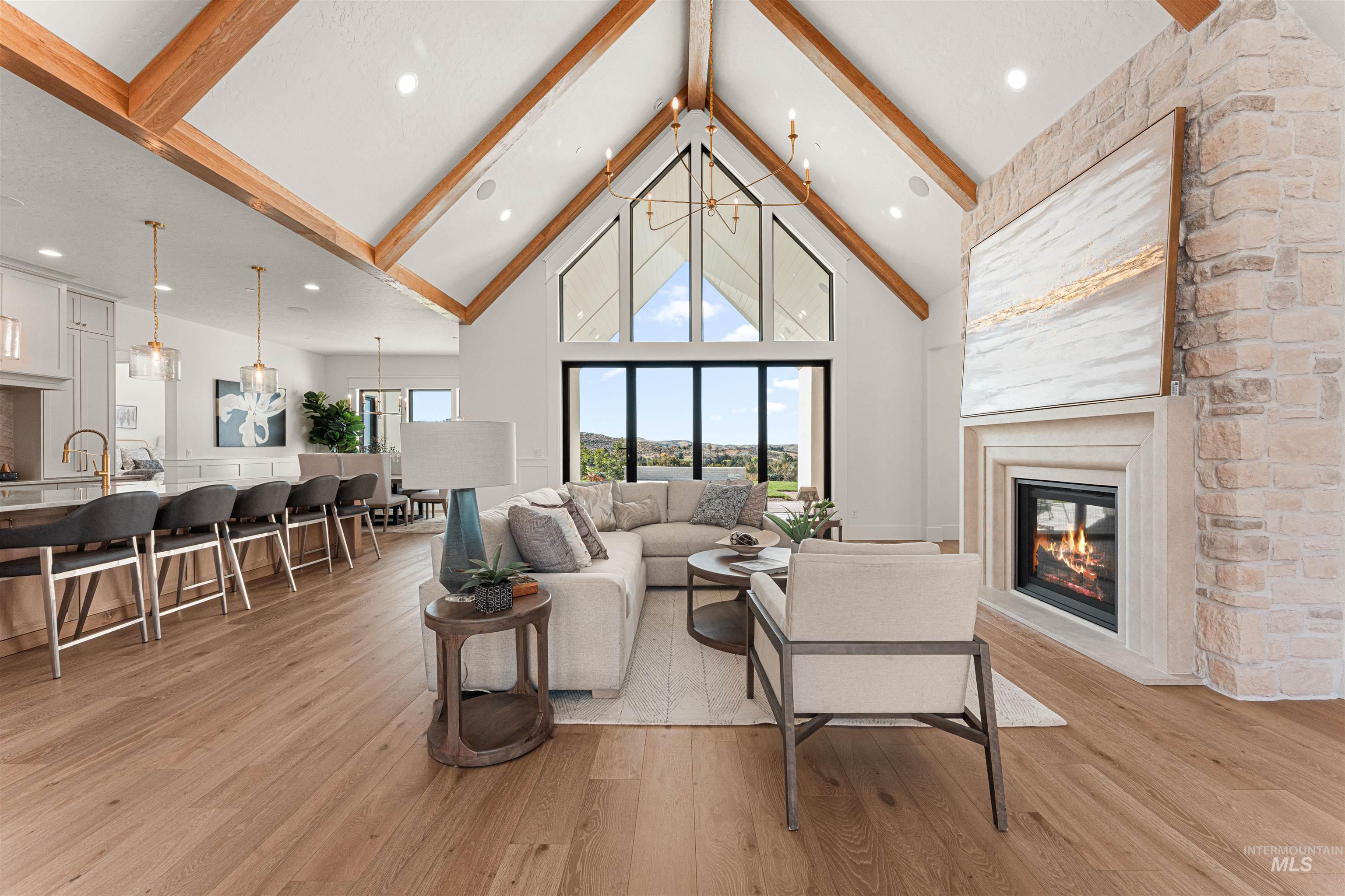 Living area with beam ceiling, high vaulted ceiling, light wood-style flooring, a chandelier, and a fireplace