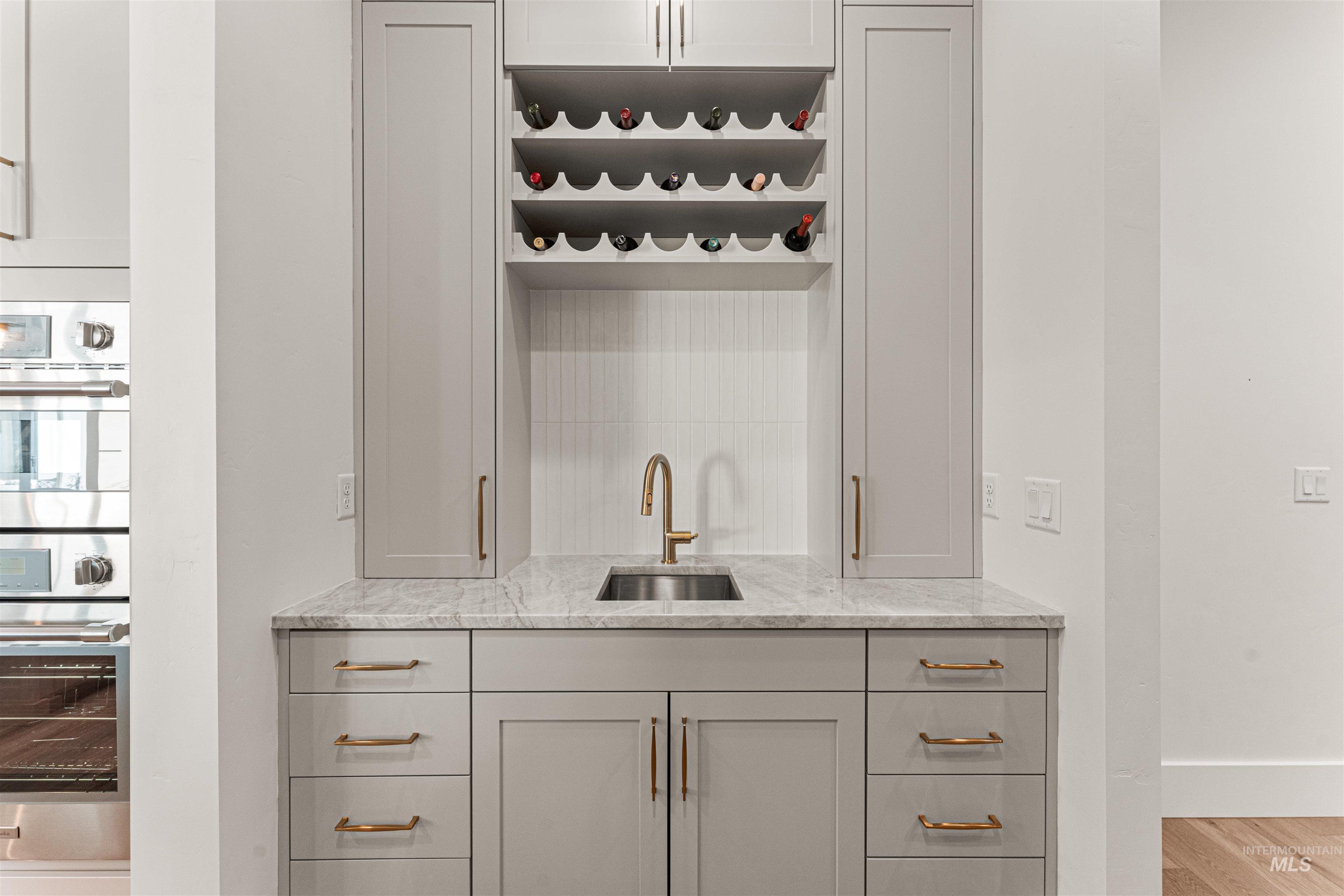 Bar area featuring light stone countertops, gray cabinetry, double oven, light wood-style floors, and open shelves
