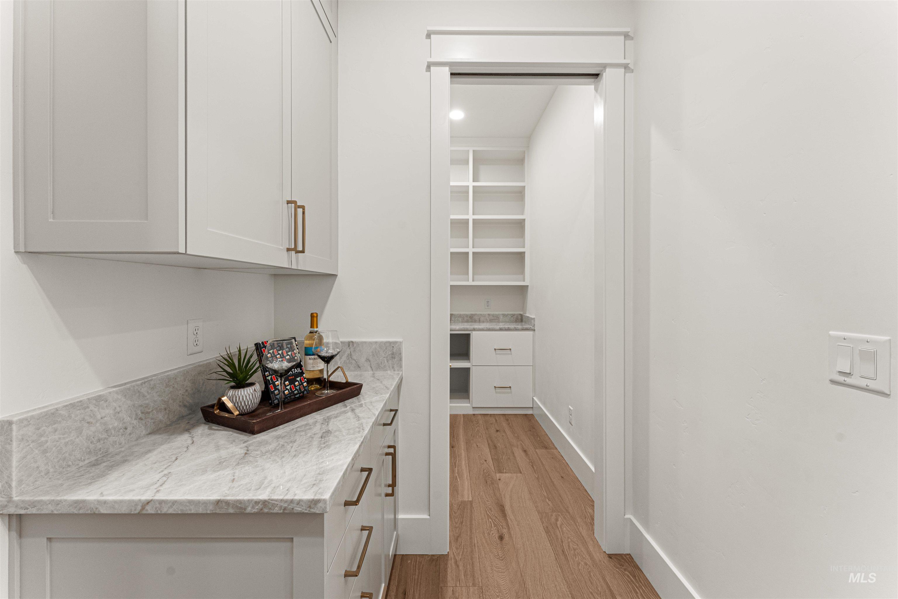 Bar area with light wood-type flooring, light stone counters, and white cabinetry