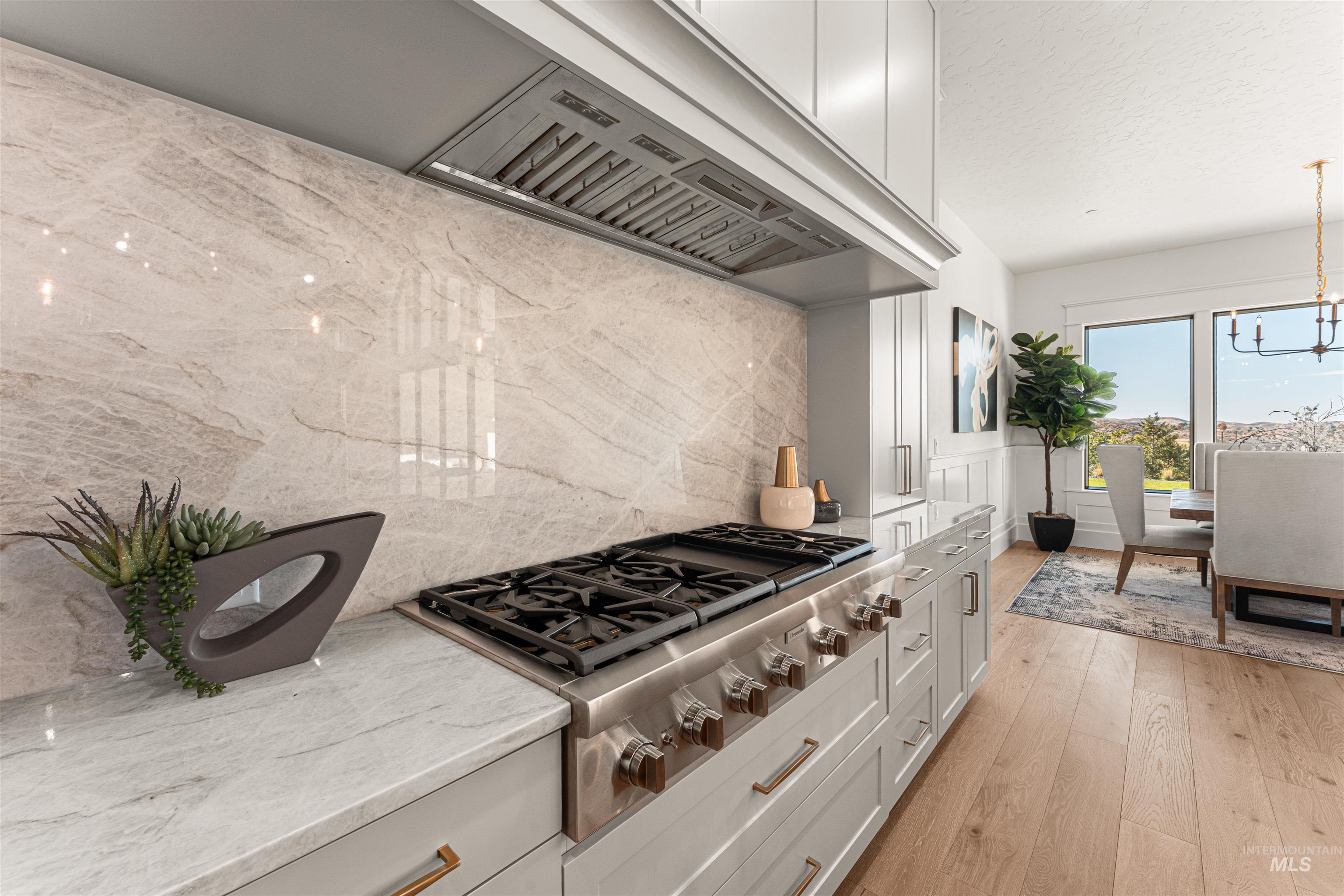 Kitchen featuring light wood-style flooring, light stone countertops, custom exhaust hood, stainless steel gas stovetop, and a chandelier