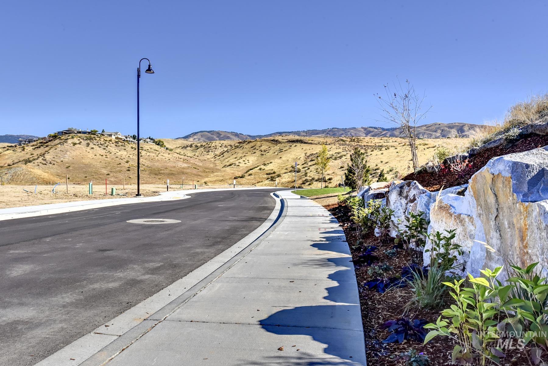 View of asphalt street with sidewalks, a mountain view, street lighting, and curbs