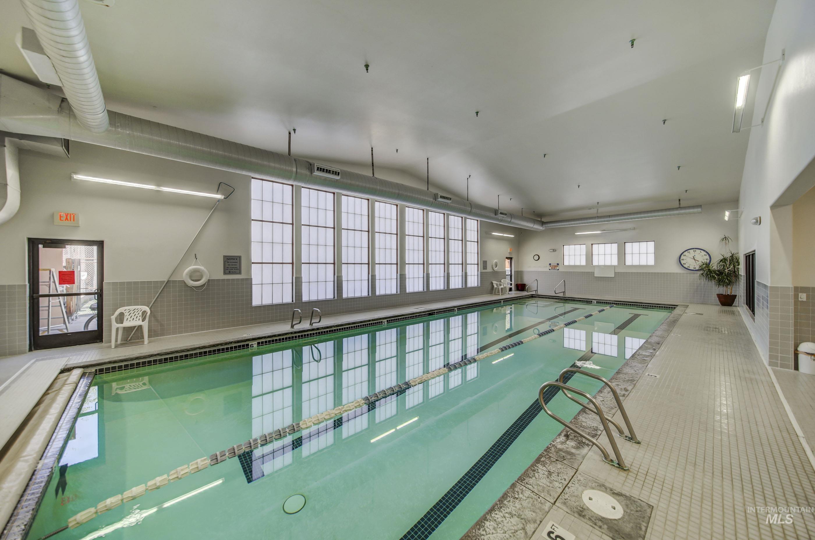 Indoor lap pool featuring multiple swim lanes, a tiled perimeter deck, and extensive natural light from large transom windows