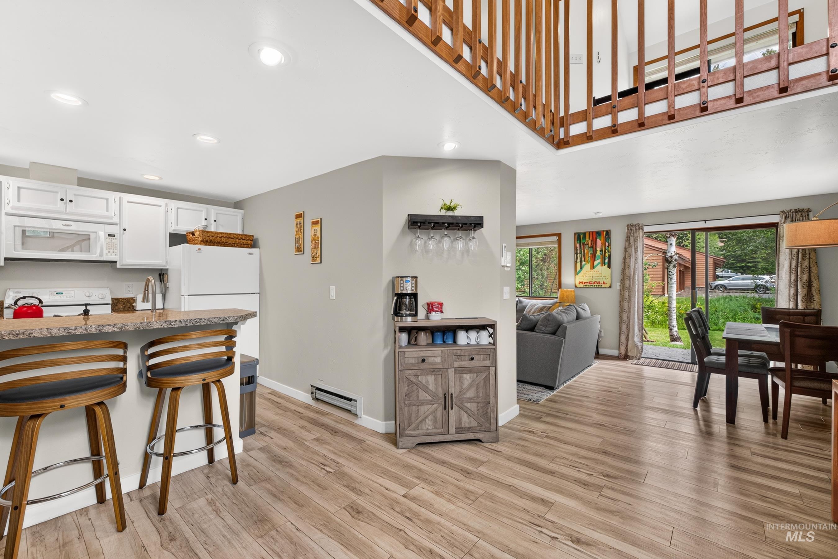 Open concept living area featuring wood-finish flooring and a kitchen with white cabinetry and a breakfast bar