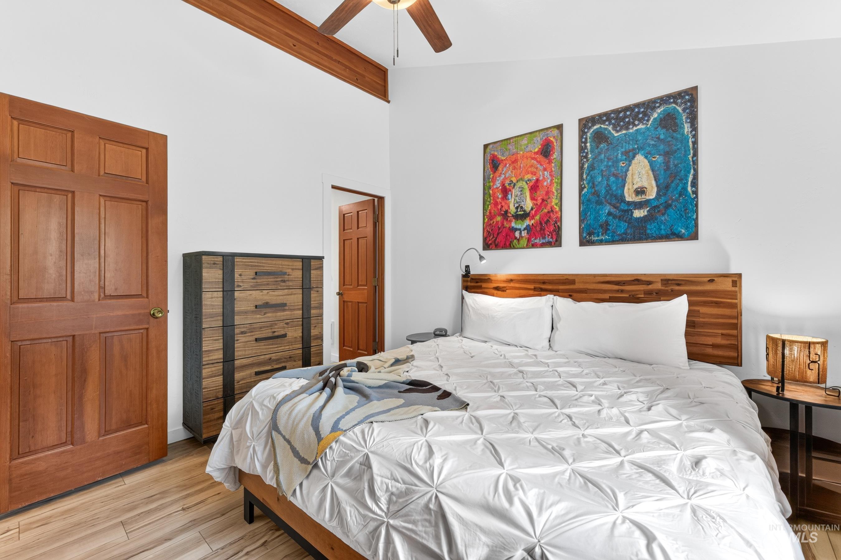 Bedroom featuring a wood-panel headboard, wood-finish flooring, and a ceiling fan with light fixture