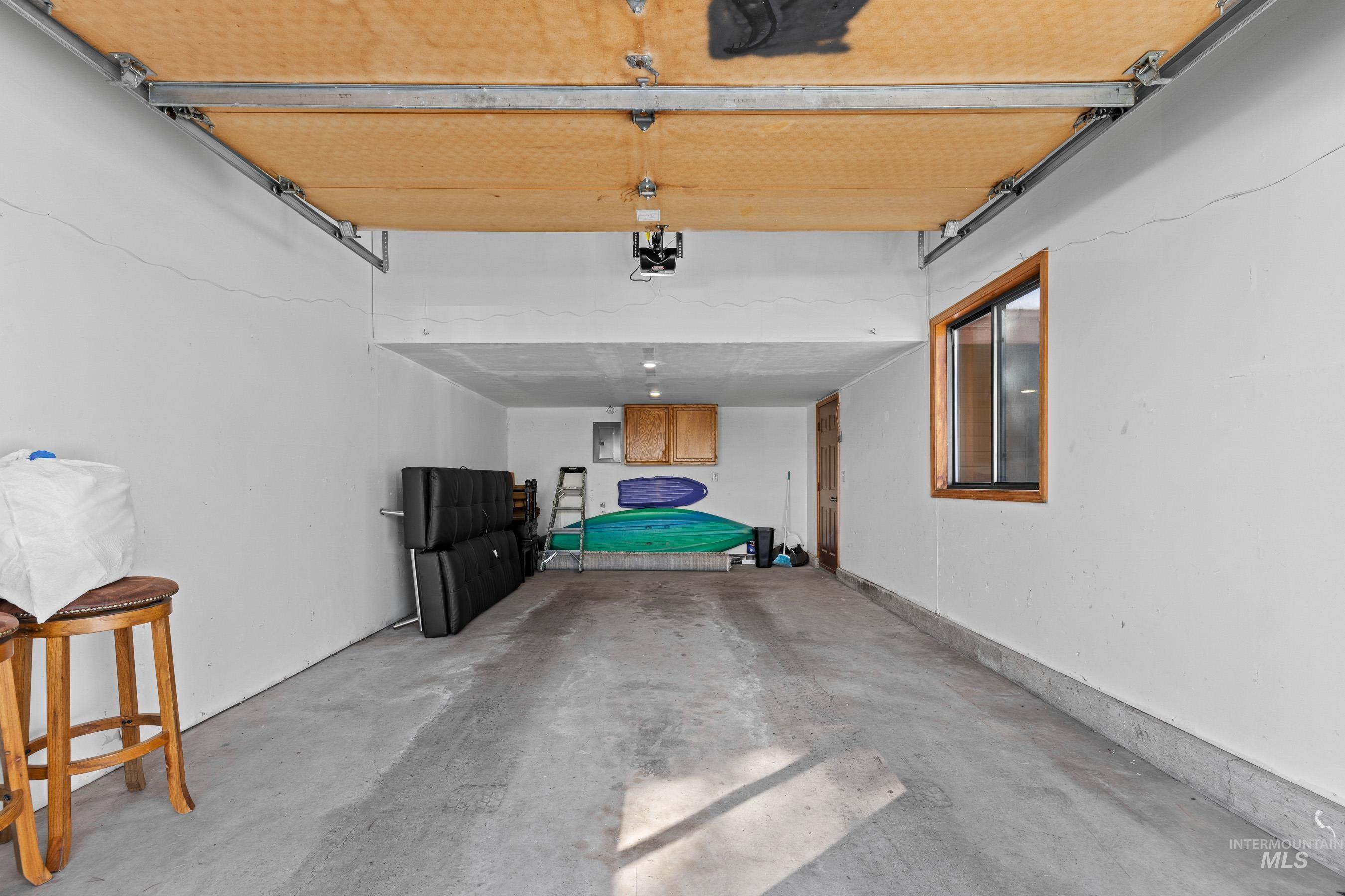 Spacious garage featuring a concrete floor, painted white walls, a wood-framed window, overhead lighting, and wood-finish cabinetry