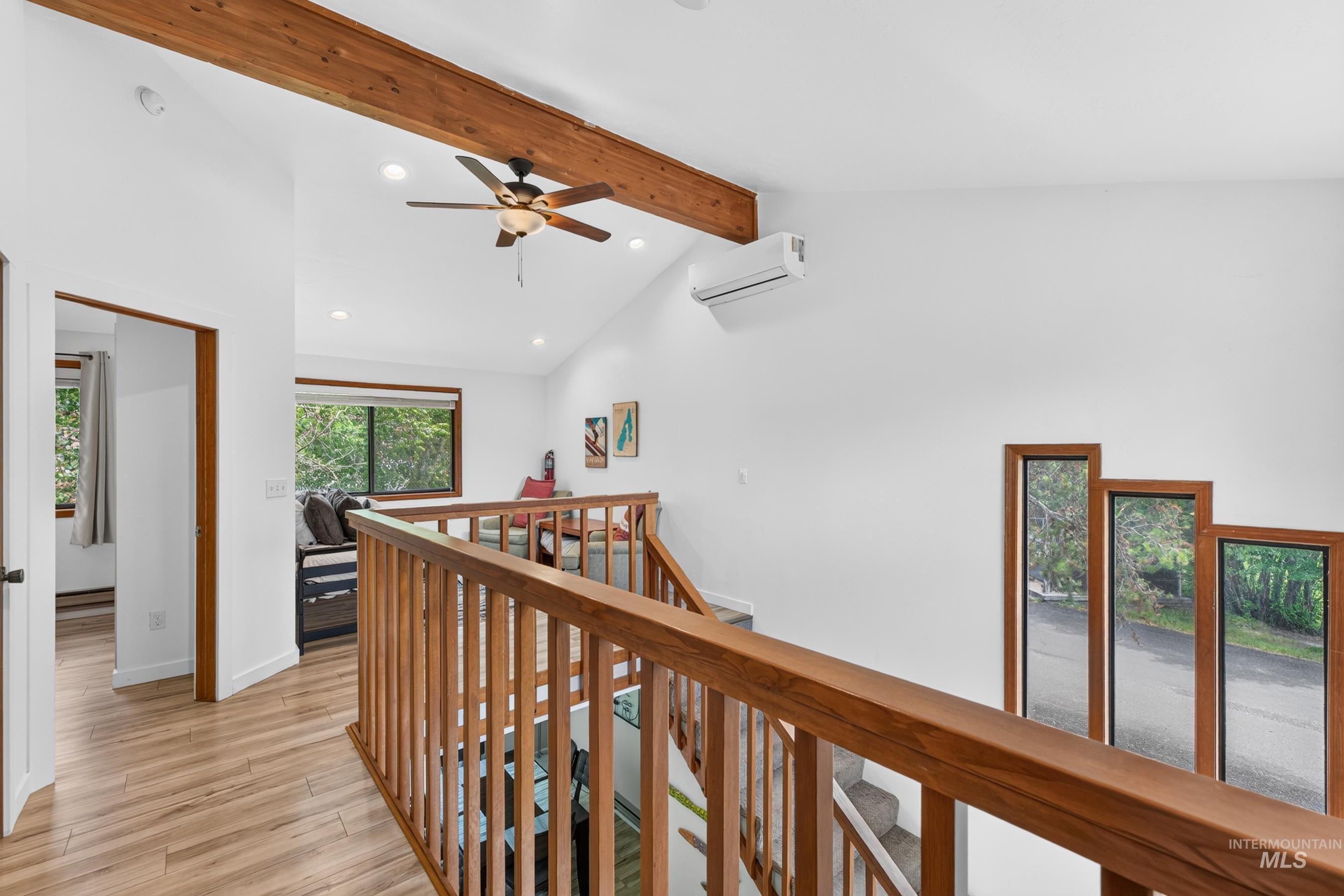 Vaulted ceilings with exposed wood beams, wood-finish flooring, and a contemporary ceiling fan