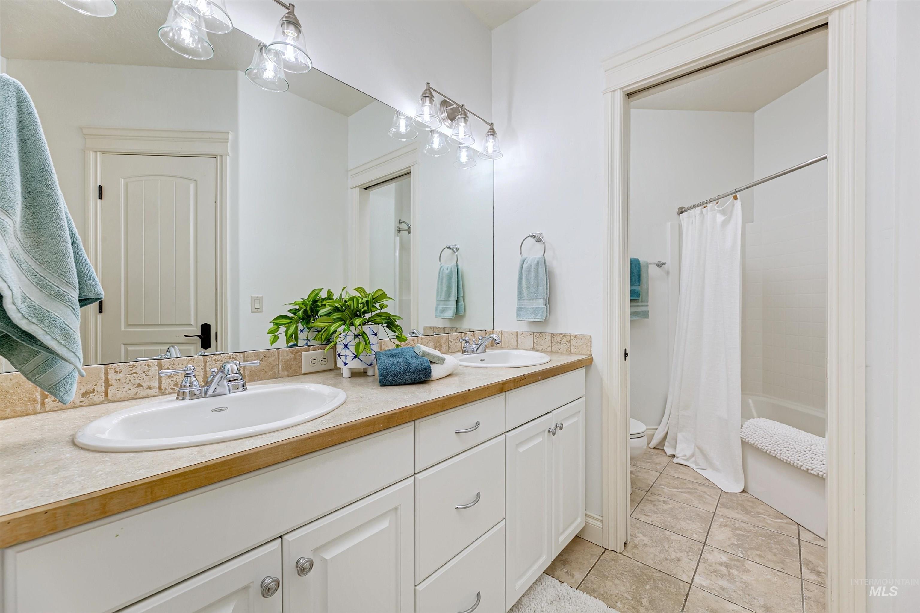 Bathroom featuring shower / tub combo with curtain, light tile patterned flooring, and double vanity