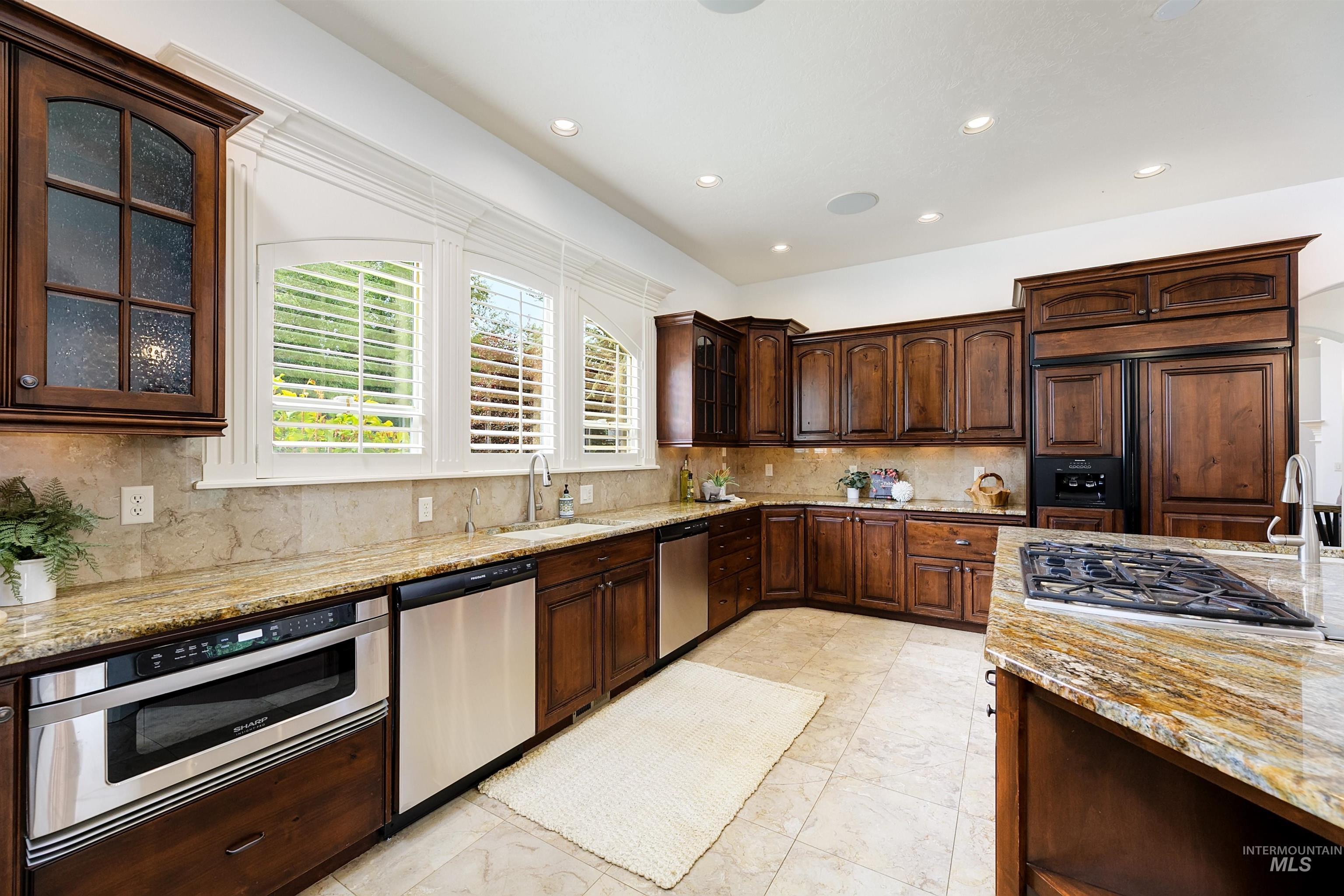Kitchen featuring glass insert cabinets, dark brown cabinets, tasteful backsplash, light stone countertops, and recessed lighting