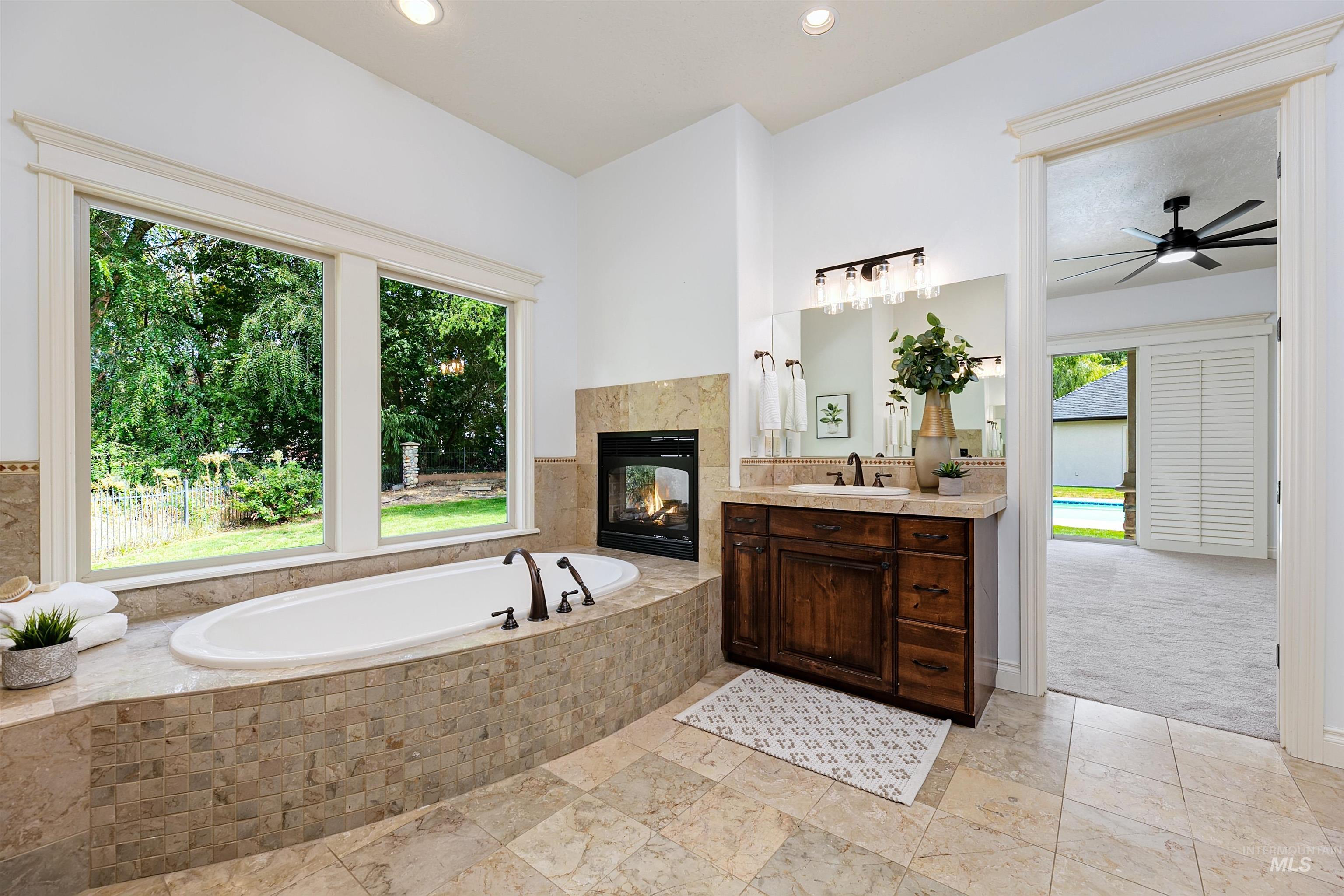 Full bathroom with vanity, a tiled fireplace, a garden tub, recessed lighting, and a ceiling fan