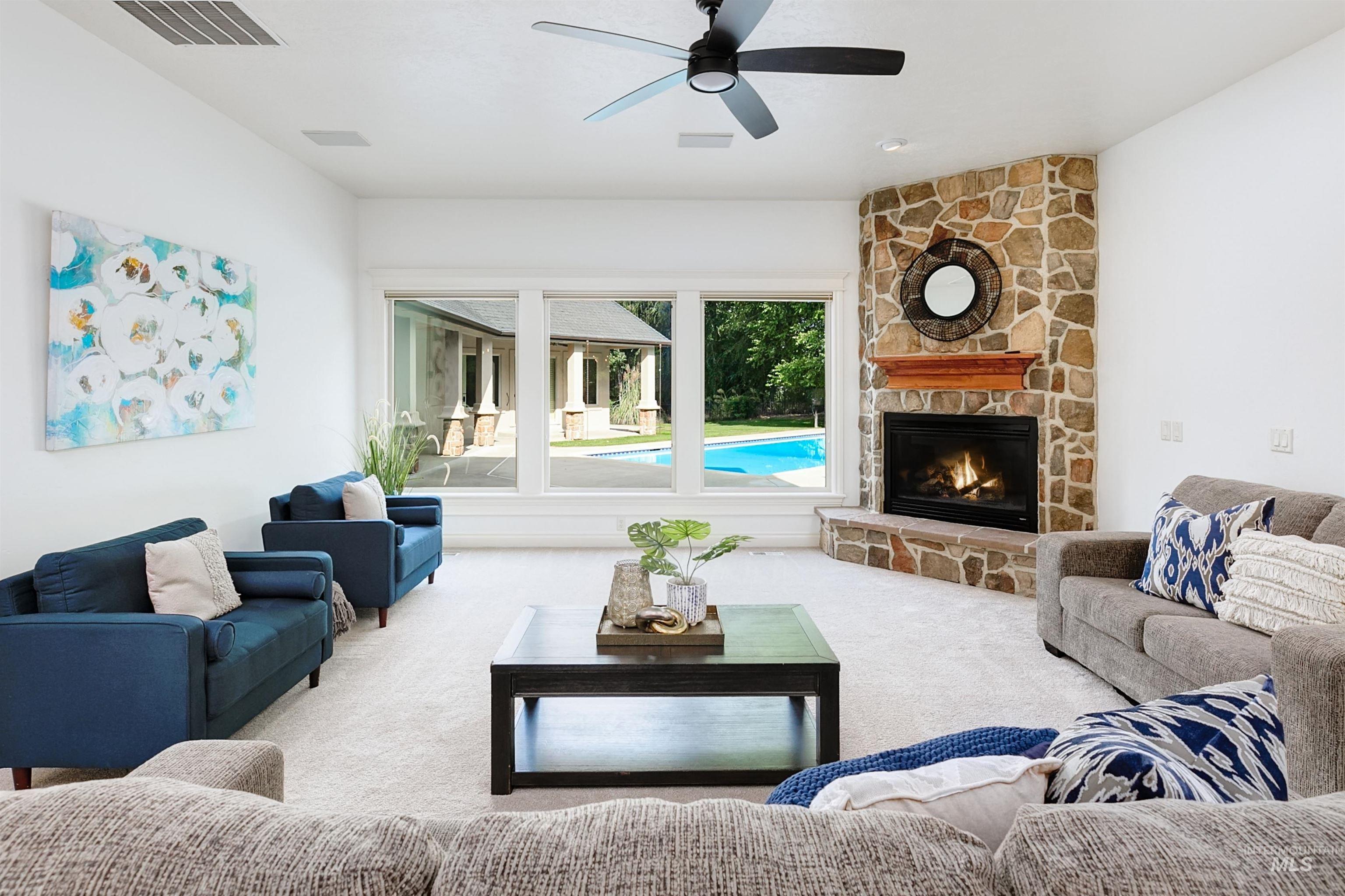 Living room with carpet, a stone fireplace, and ceiling fan