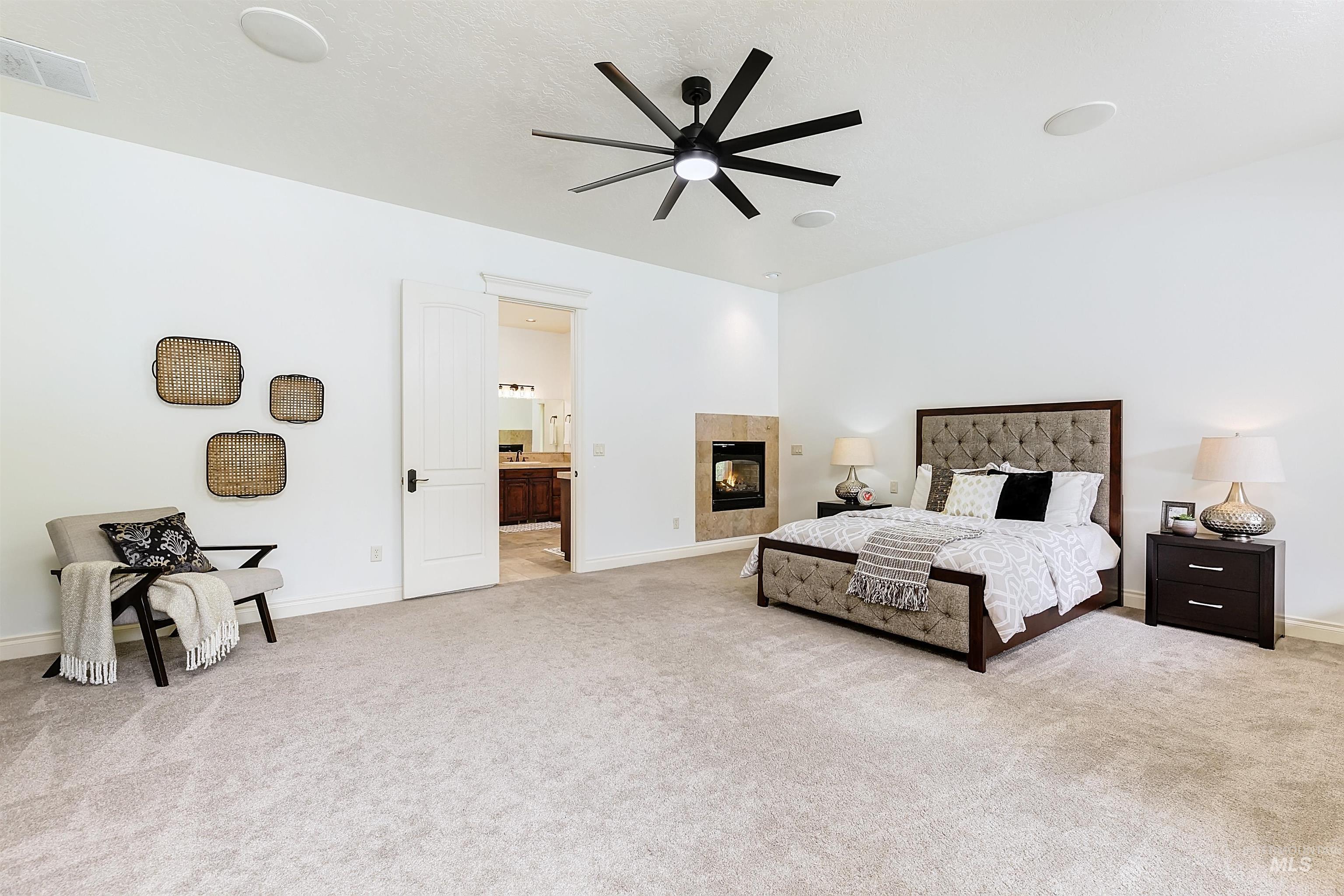 Bedroom featuring a tile fireplace, light carpet, ceiling fan, and ensuite bath