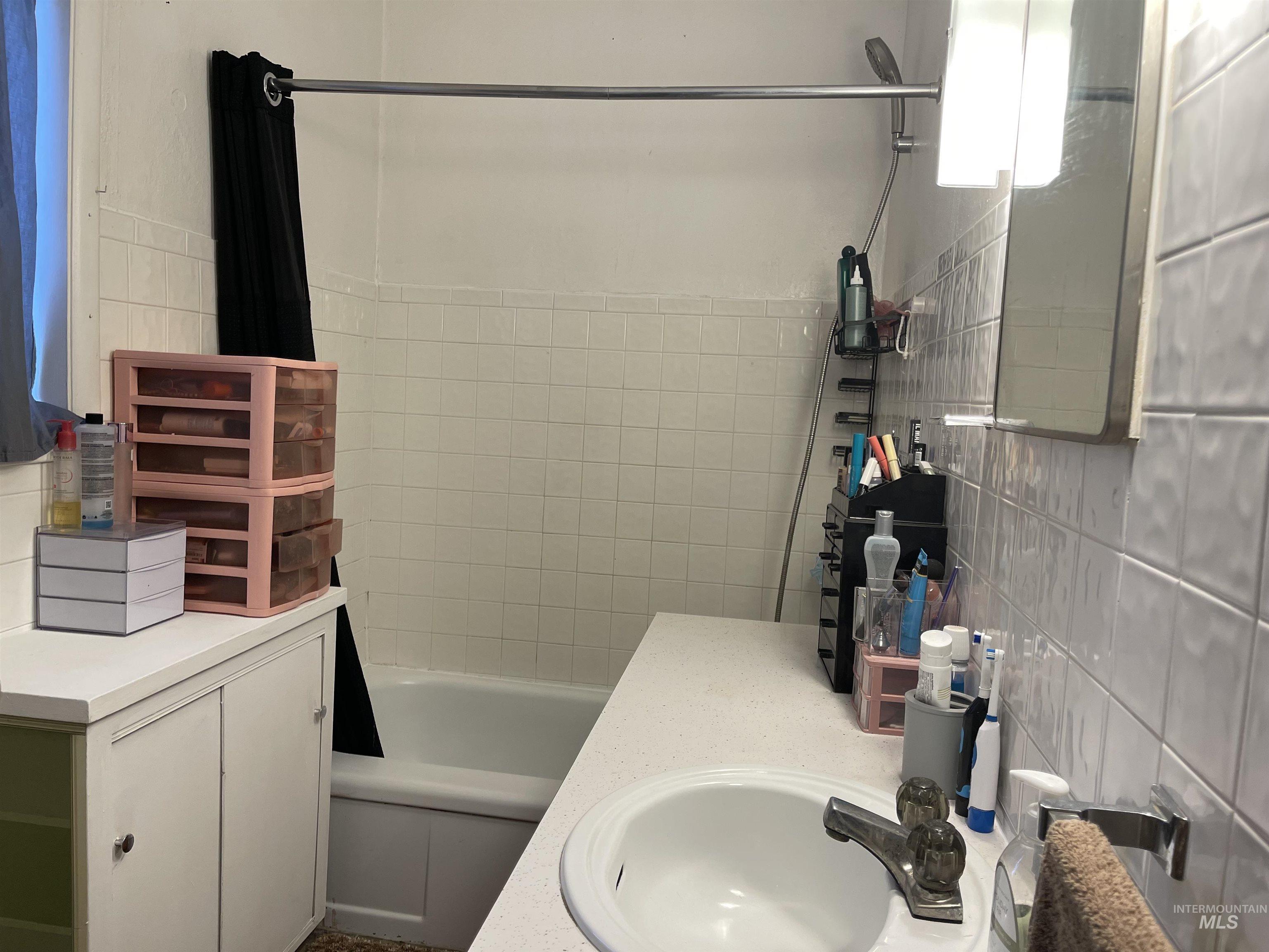 Bathroom featuring shower / bath combination with curtain, tile walls, and vanity