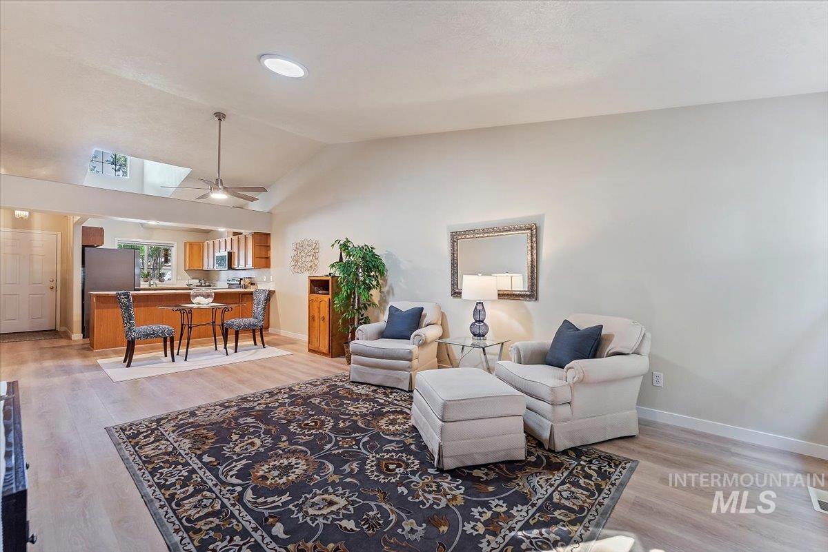 Living room featuring light wood-style floors, high vaulted ceiling, a skylight, and ceiling fan