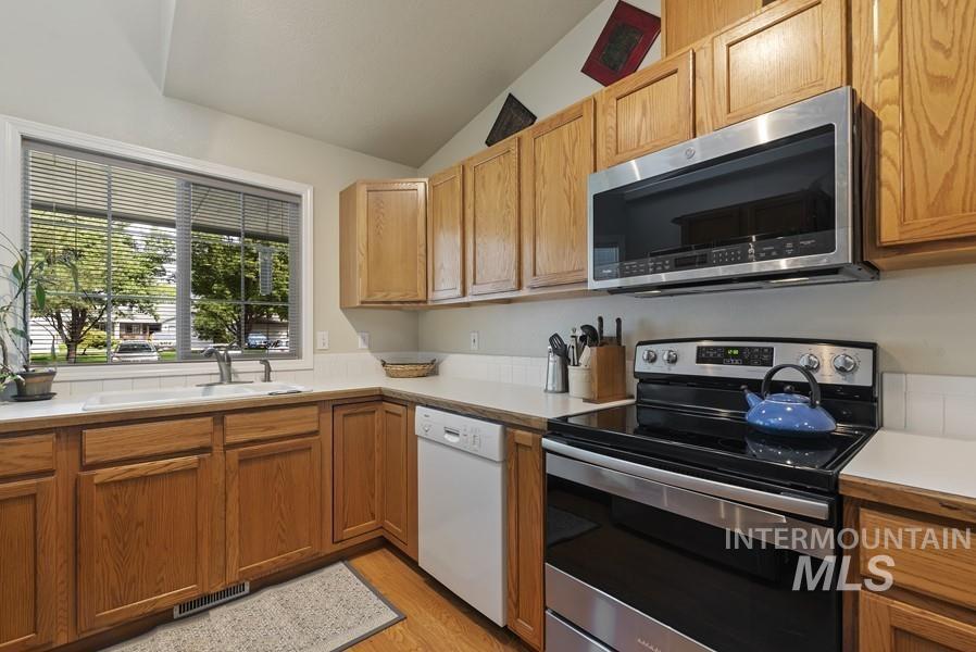 Kitchen featuring appliances with stainless steel finishes, light countertops, vaulted ceiling, light wood finished floors, and brown cabinetry