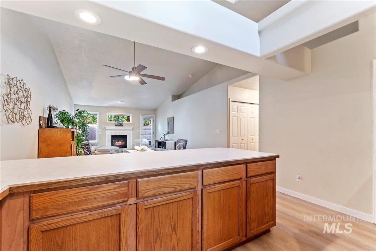 Kitchen featuring light countertops, vaulted ceiling, a lit fireplace, light wood-style floors, and recessed lighting