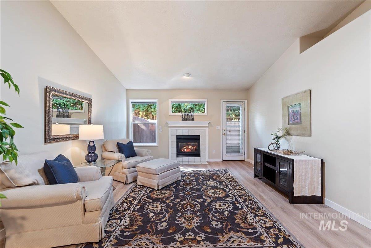 Living area featuring light wood finished floors, a tile fireplace, plenty of natural light, and vaulted ceiling