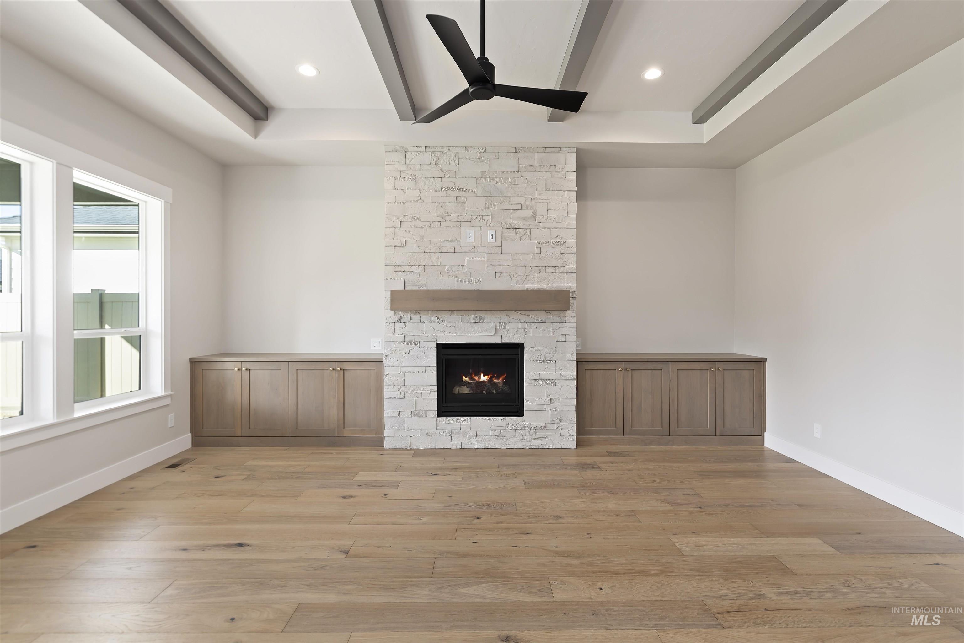 Unfurnished living room featuring beam ceiling, light wood-style floors, ceiling fan, a stone fireplace, and recessed lighting