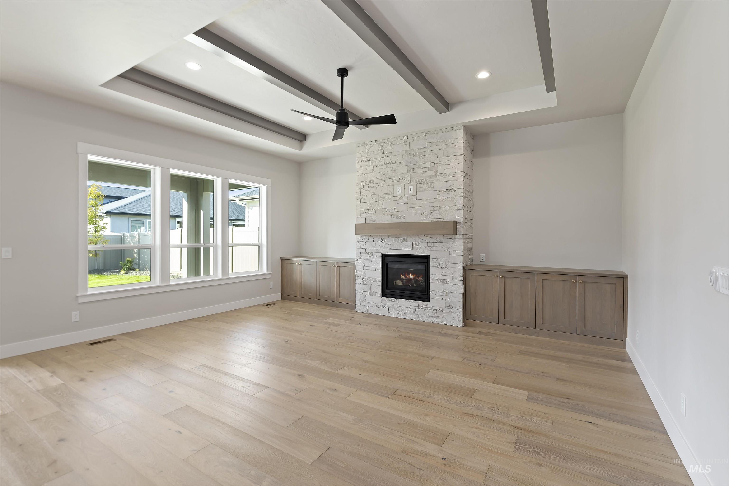 Unfurnished living room with a ceiling fan, beamed ceiling, a tray ceiling, light wood-style floors, and a fireplace