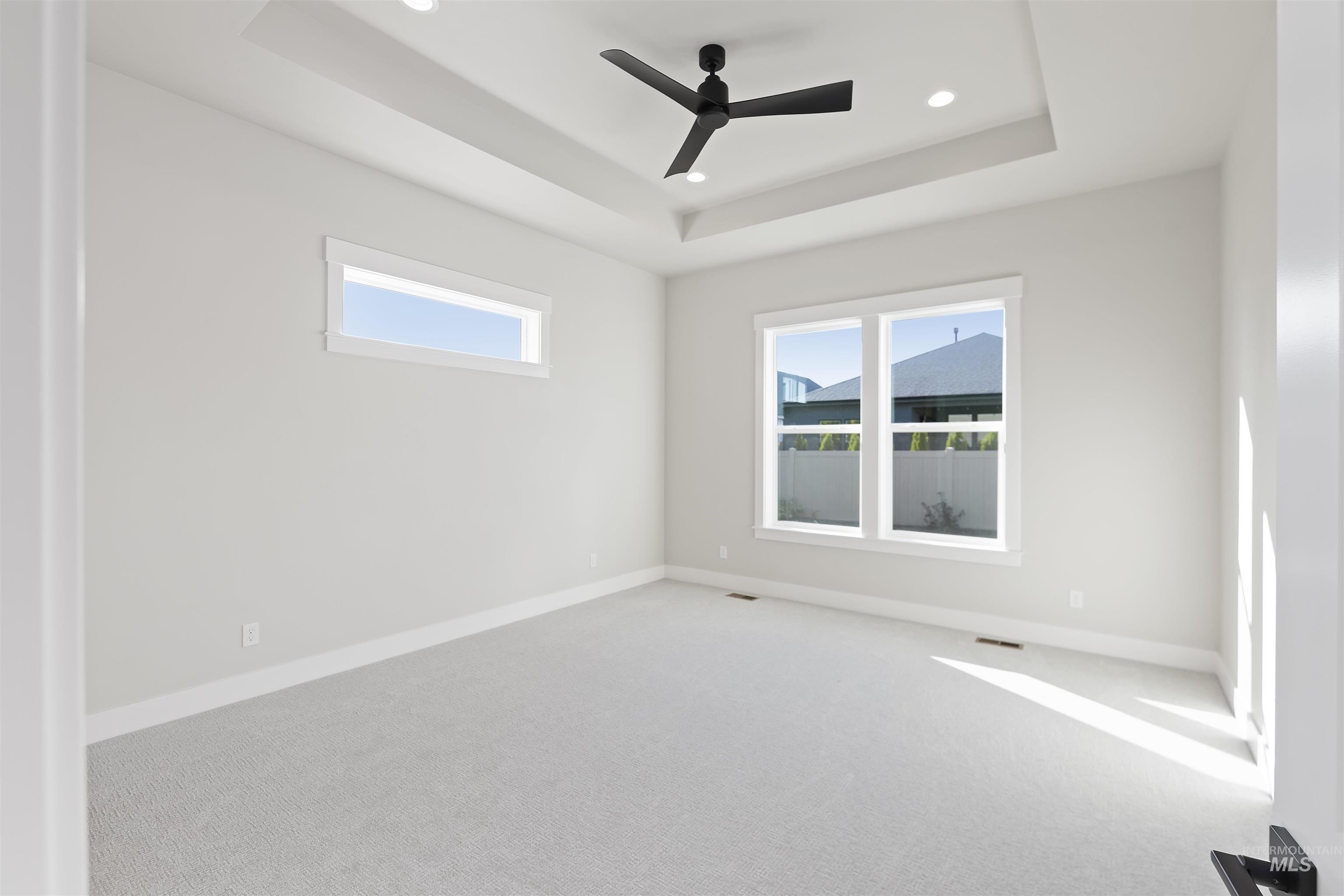 Carpeted spare room featuring a tray ceiling, ceiling fan, healthy amount of natural light, and recessed lighting