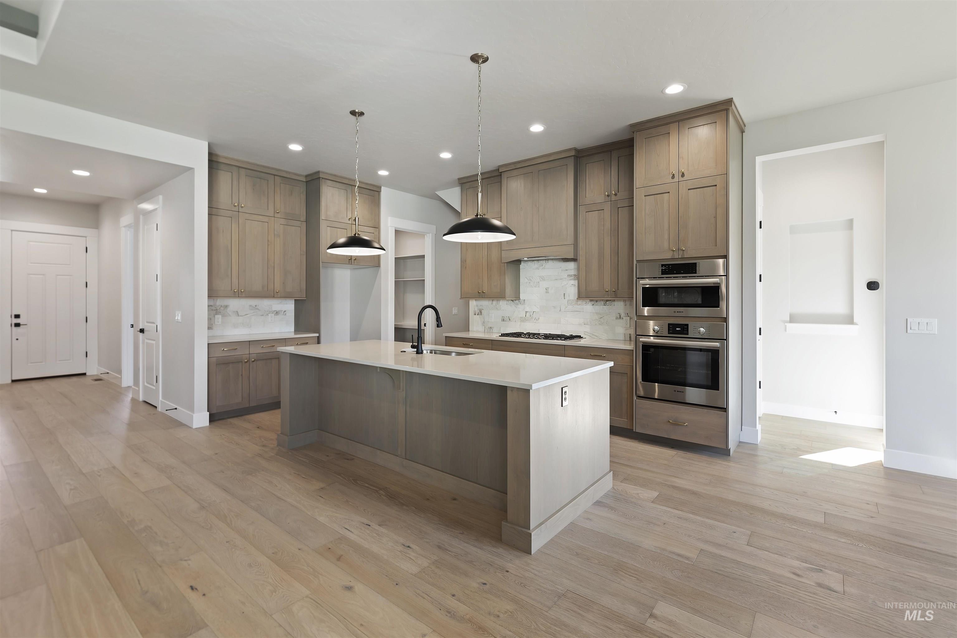 Kitchen with backsplash, decorative light fixtures, light stone countertops, a kitchen island with sink, and light wood finished floors