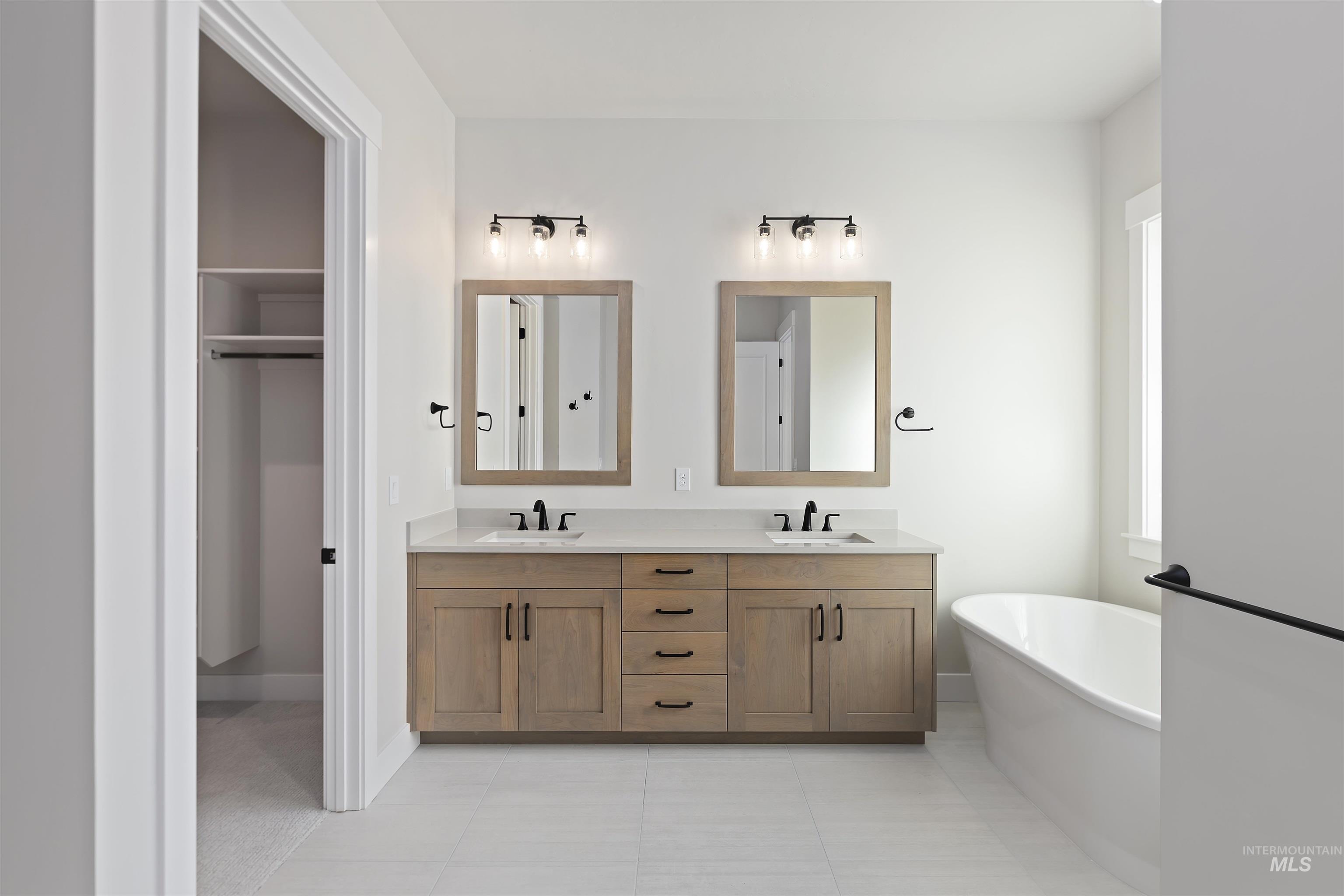 Full bath with a freestanding bath, double vanity, light tile patterned floors, and a walk in closet