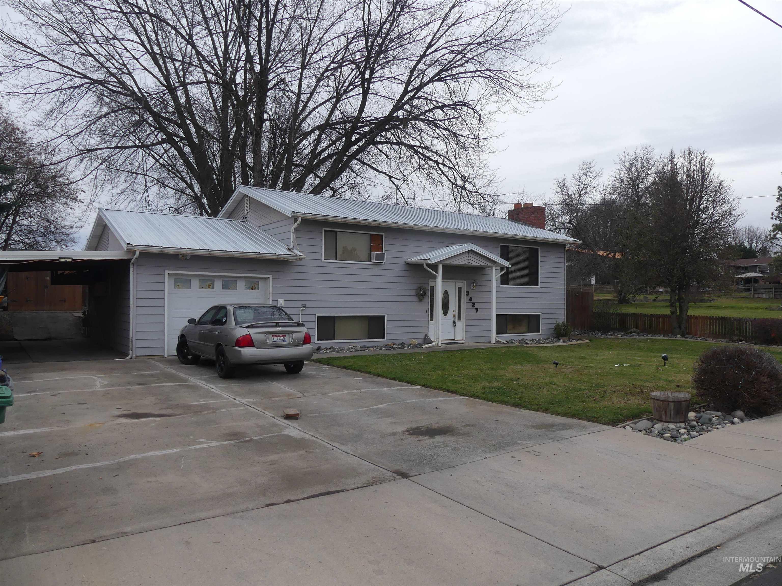 Split foyer home featuring concrete driveway, a front lawn, a chimney, an attached carport, and a garage